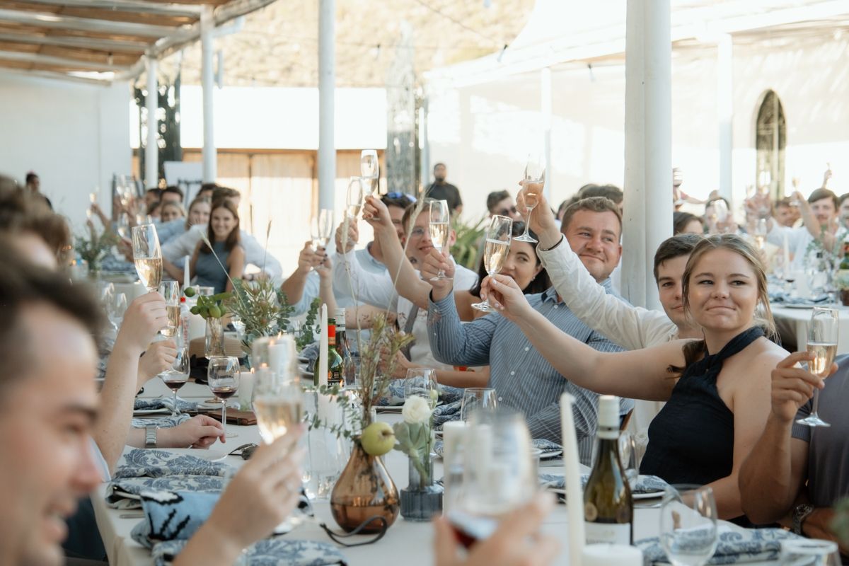 Wedding reception guests raising glasses in a joyful toast, smiling and celebrating at elegantly decorated long tables.
