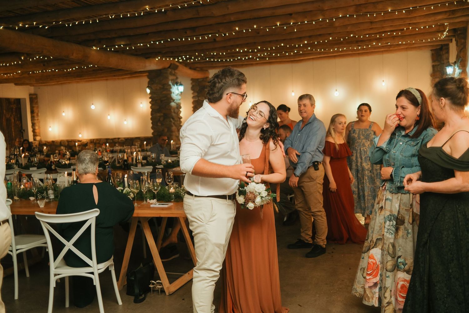 Couple sharing a romantic first dance surrounded by guests at a rustic wedding.