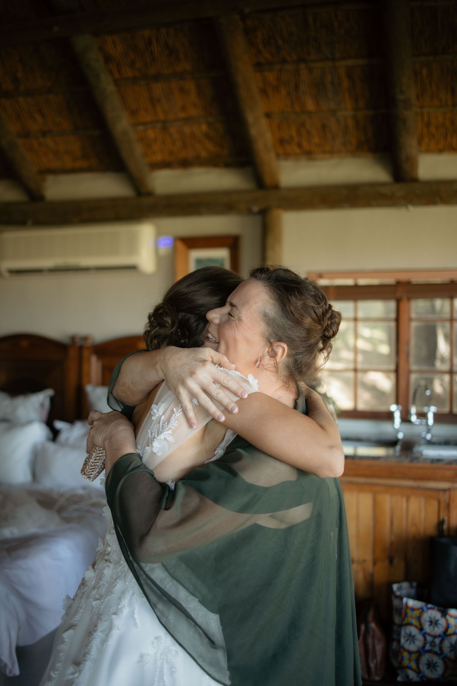 Emotional bride and older woman sharing a heartfelt hug during wedding preparations indoors.