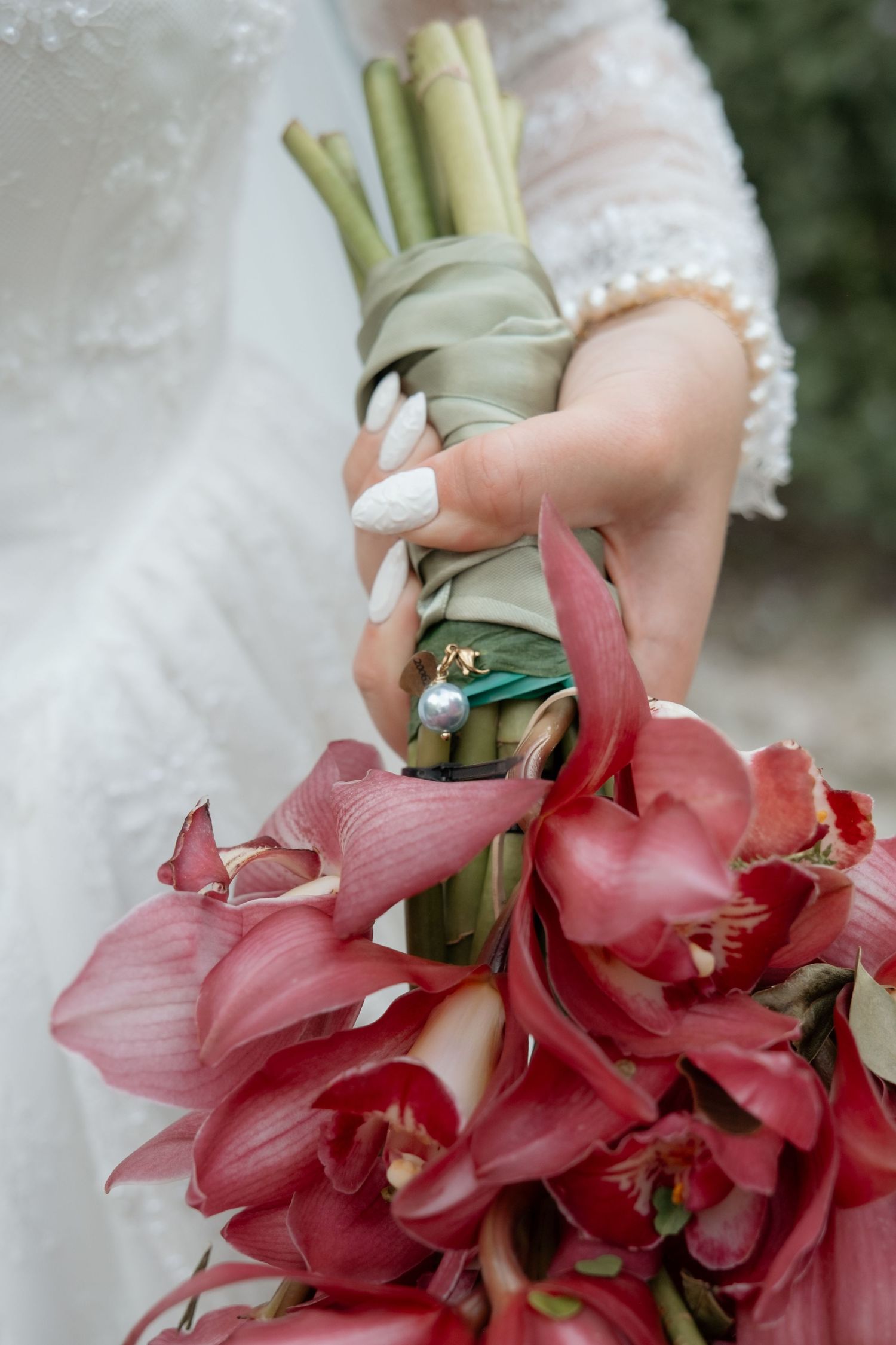 Bride holding stunning red orchid bouquet wrapped in green ribbon with pearl charm.