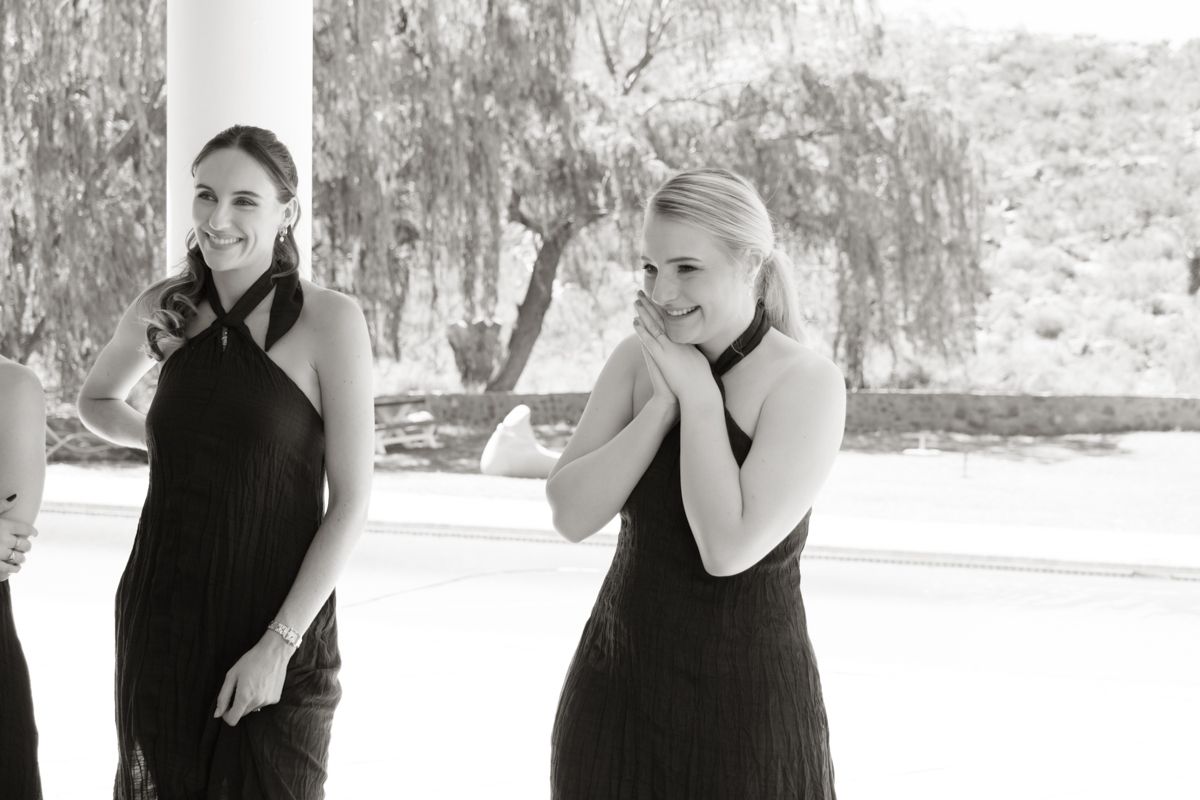 Two bridesmaids in black halter dresses share a candid moment in black and white photo.
