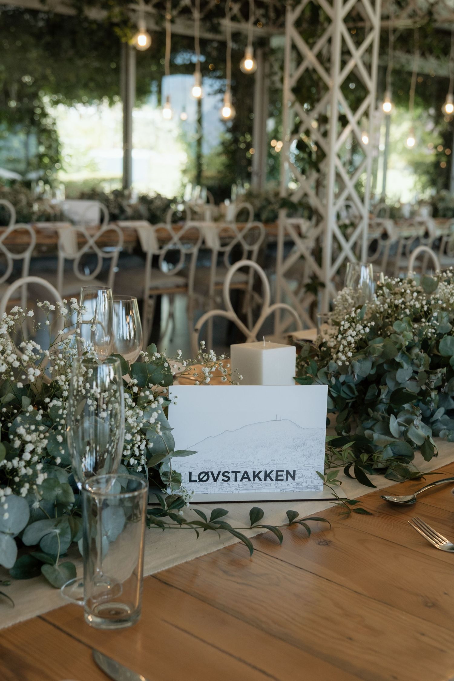 Elegant wedding reception table with eucalyptus greenery, candles, and a Lovstakken place card.