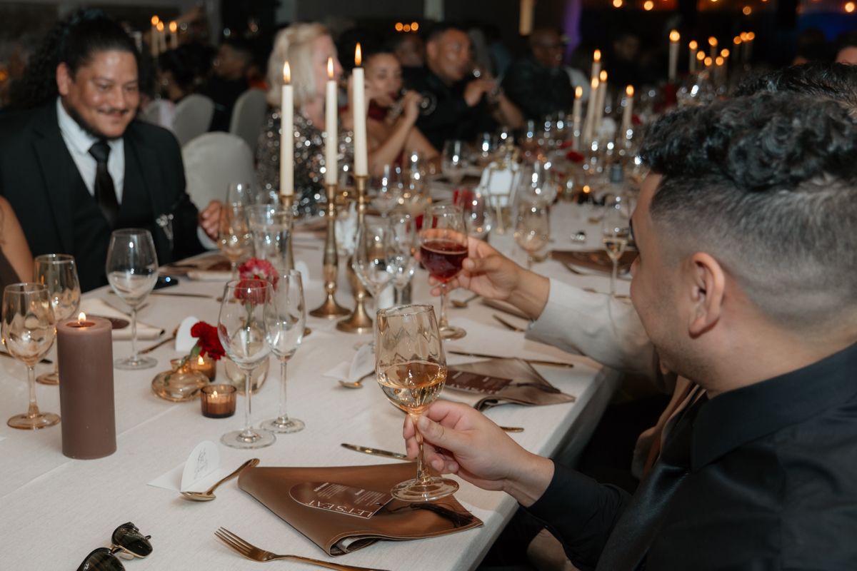 Wedding guests raising glasses in a toast at a candlelit reception dinner table.