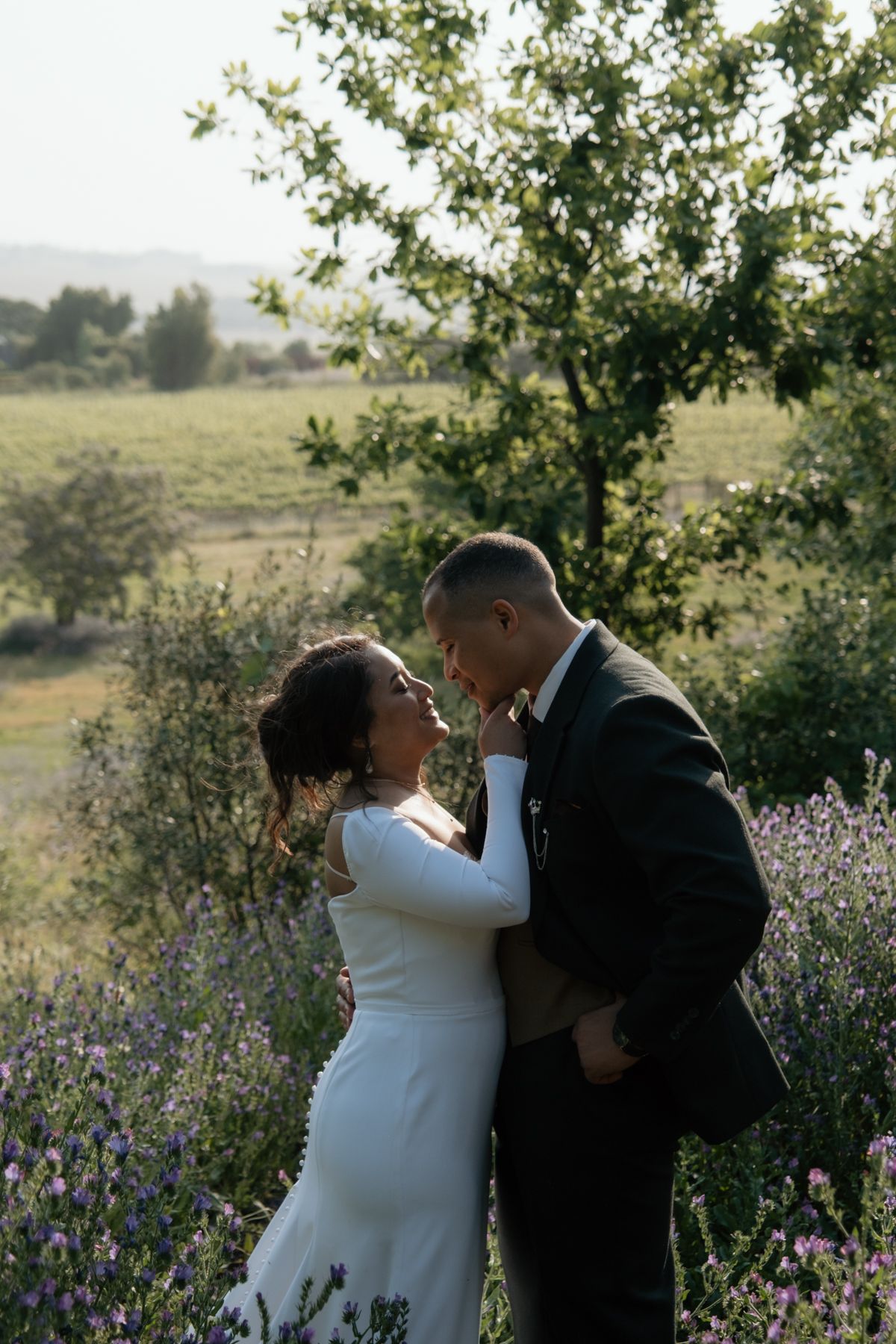 Bride and groom share a romantic almost-kiss moment surrounded by lavender flowers at golden hour.