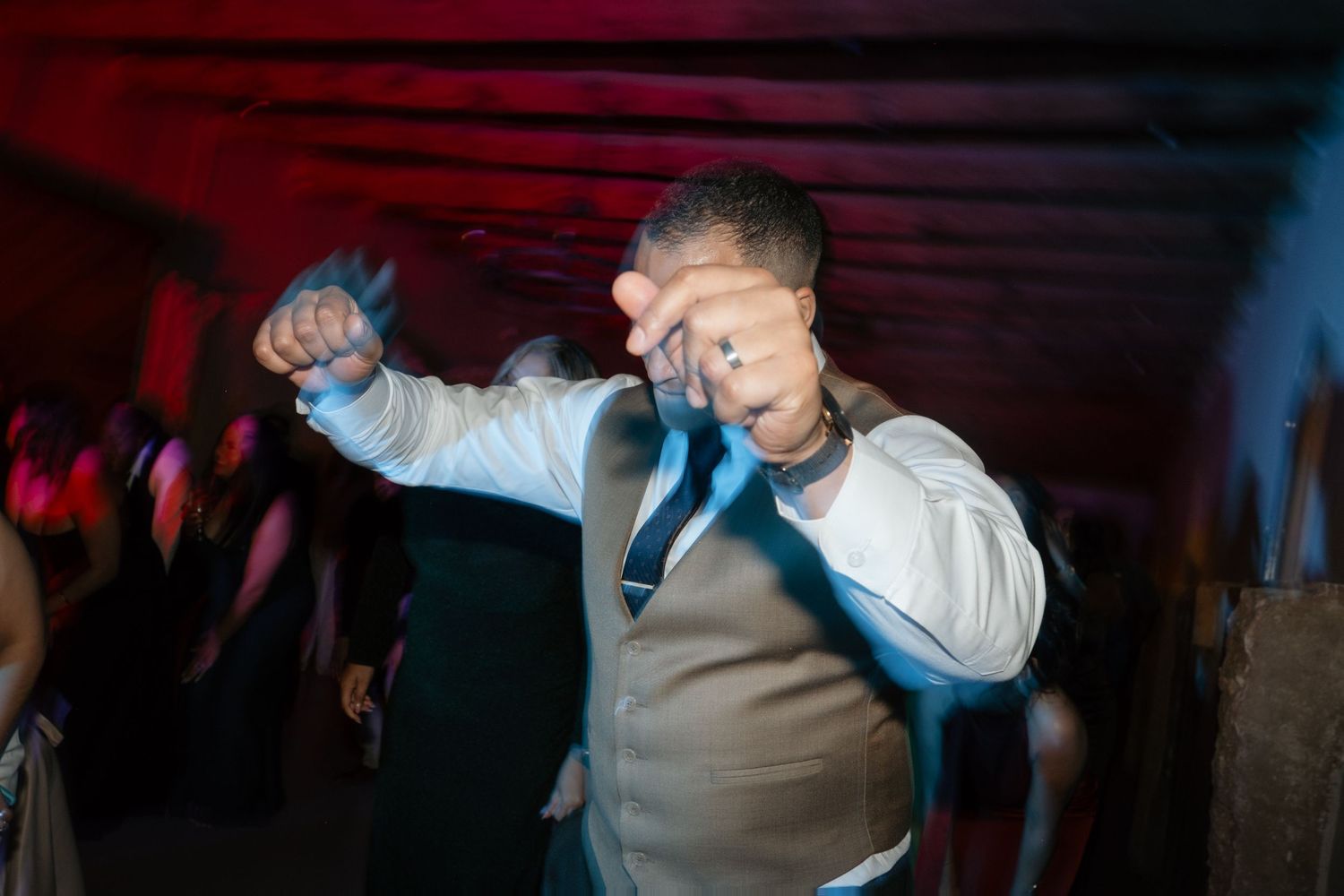 Guest dances energetically under colorful lights at lively indoor wedding reception party.