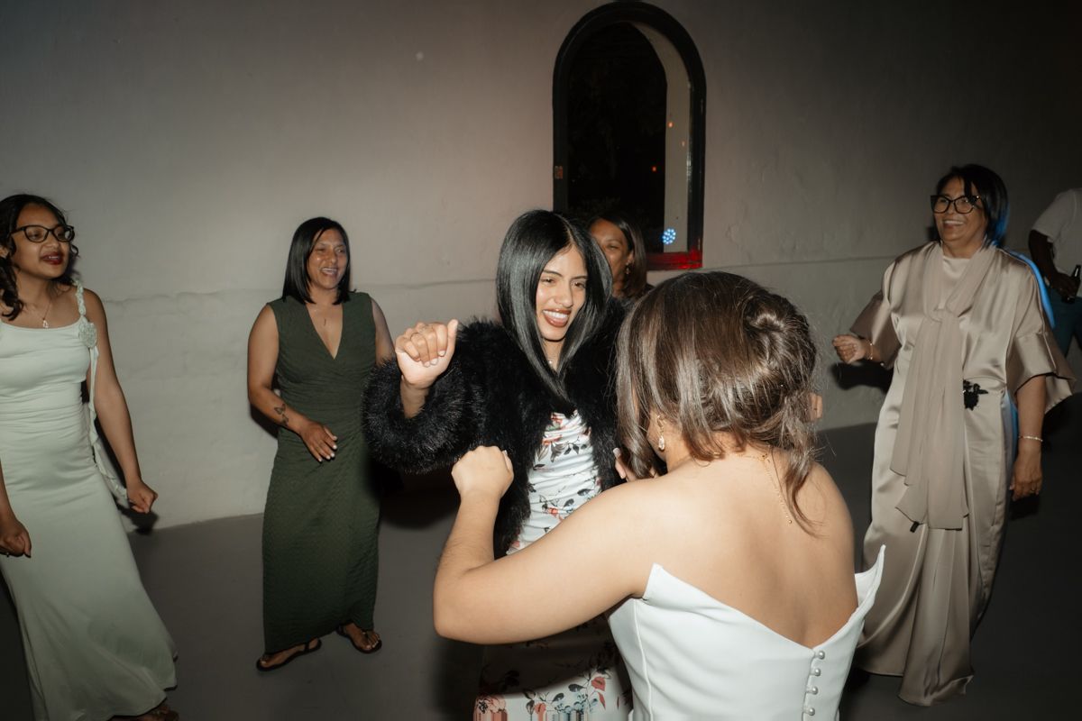 Young woman with long black hair dances joyfully with bride at lively wedding reception celebration.