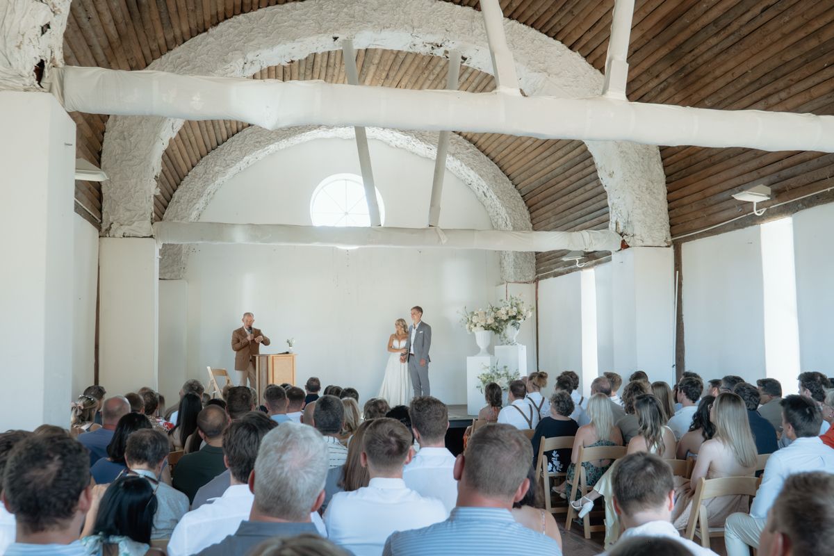 Guests seated at an elegant wedding ceremony inside a rustic white arched hall.