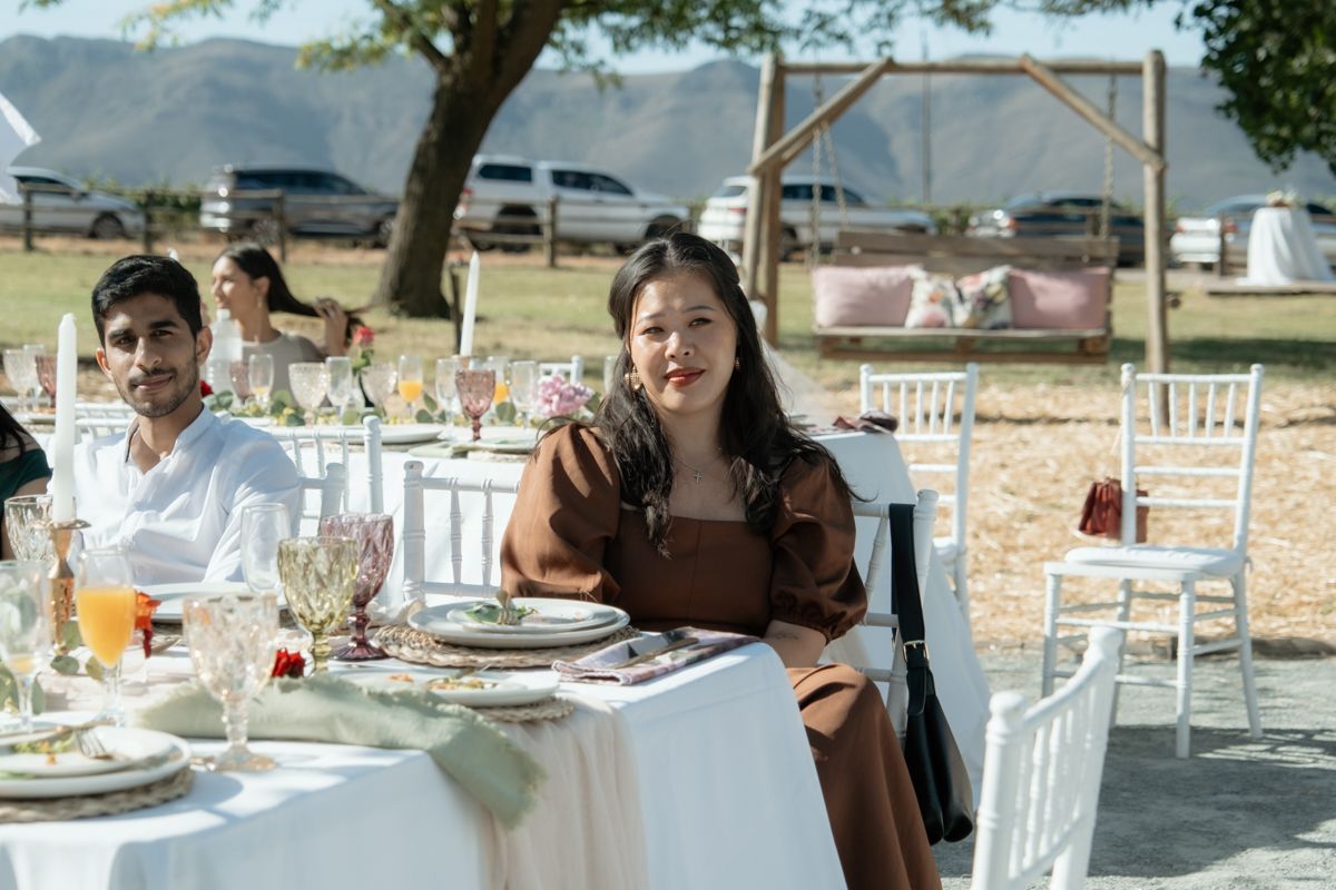 Woman in brown dress seated at elegantly set outdoor wedding reception table.