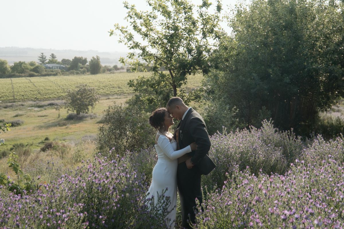 Bride and groom embrace in a stunning lavender field with scenic countryside views at golden hour.