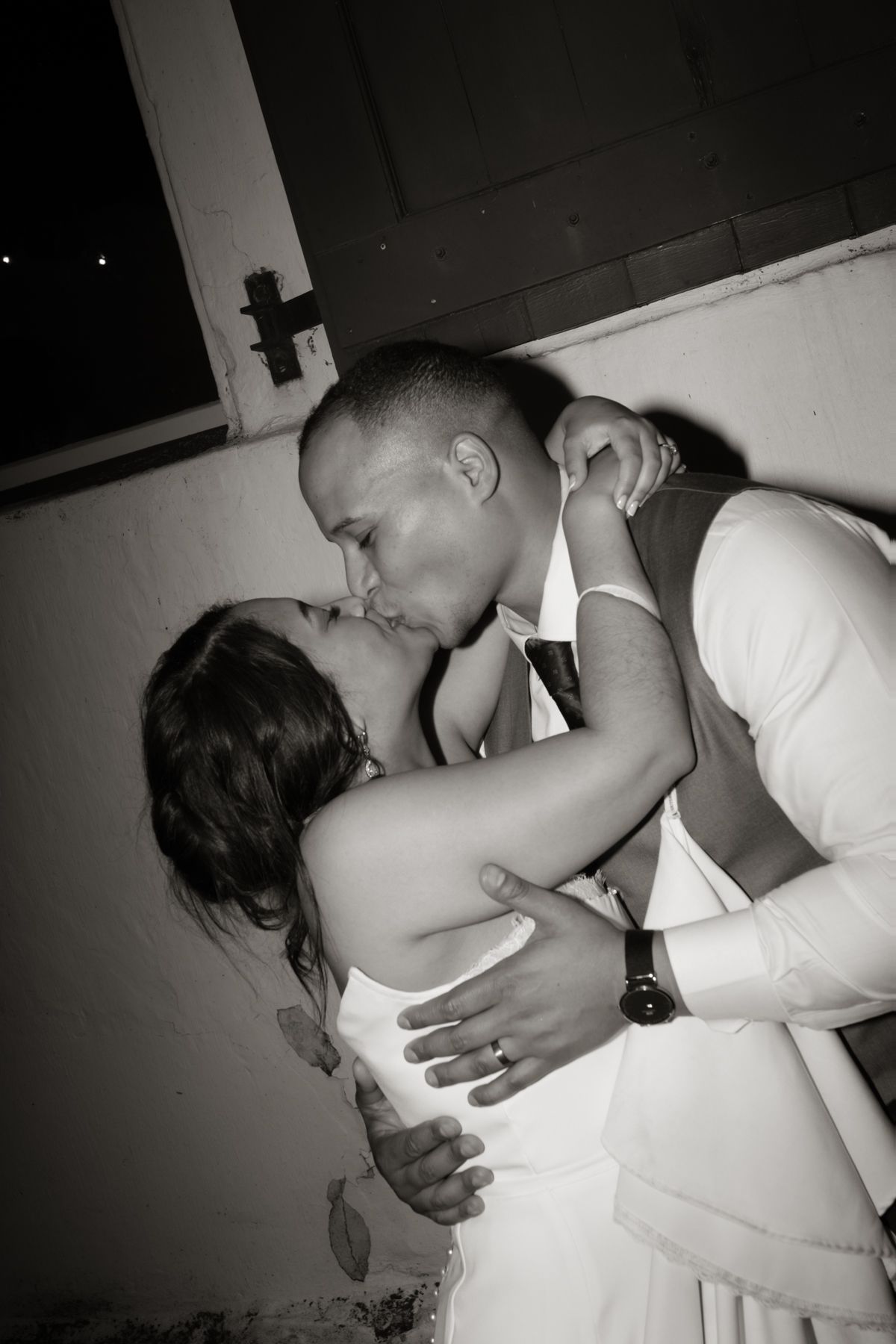 Bride and groom share passionate kiss in romantic black and white wedding night portrait.