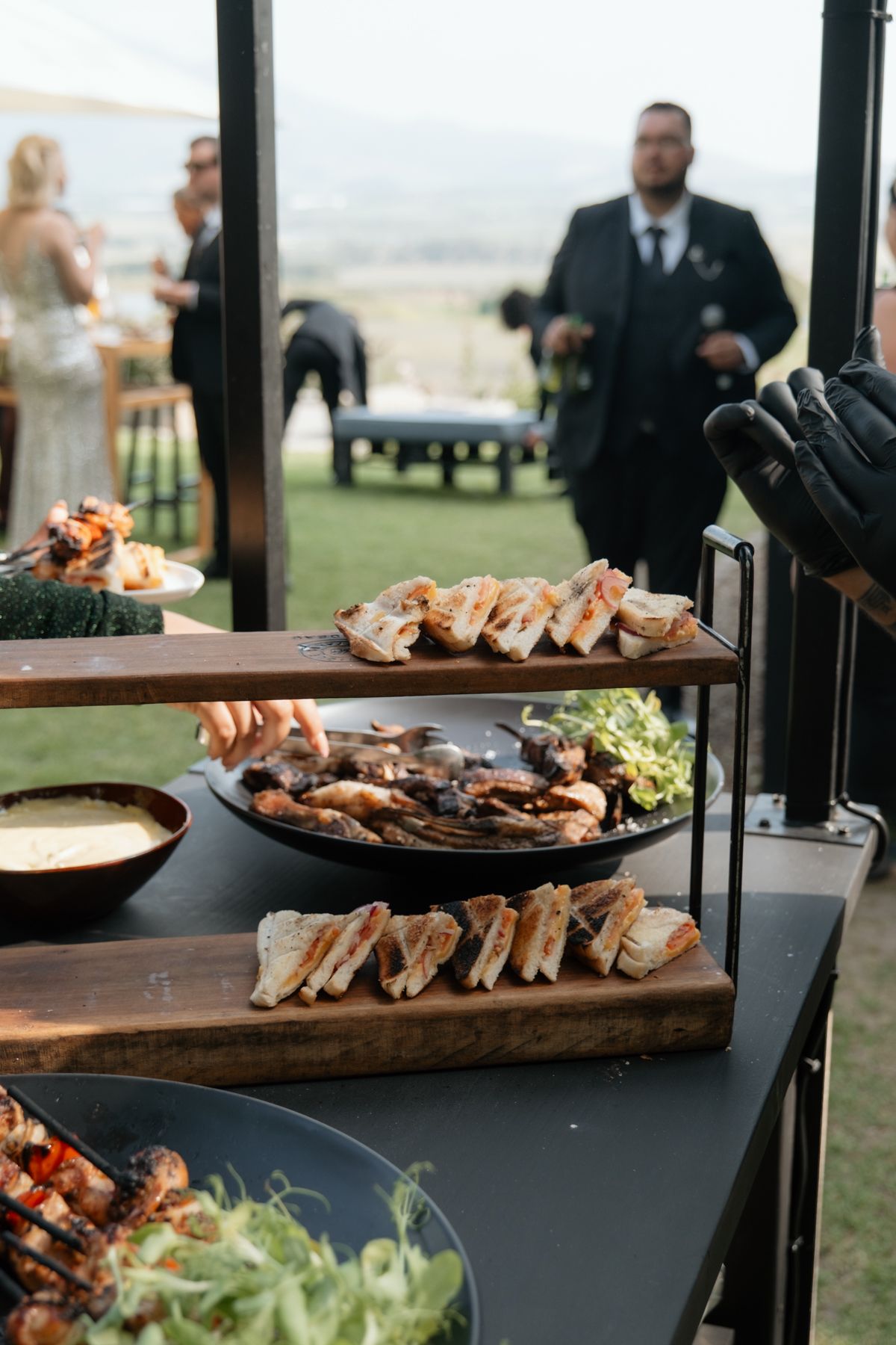 Close-up of a wedding catering spread featuring grilled meats, bread, and salads on wooden serving boards.