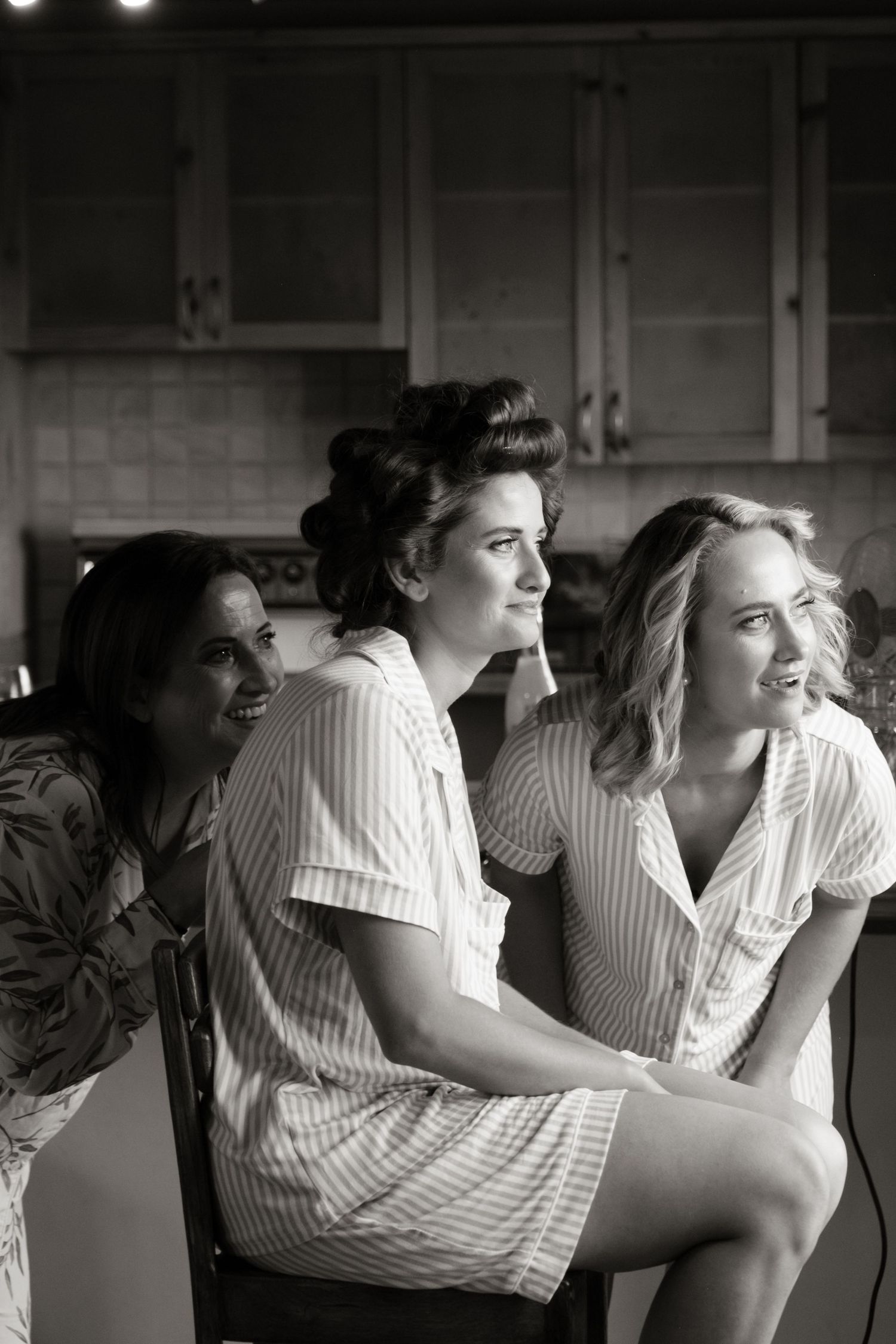Three women in striped pajamas laugh together in a kitchen during bridal party getting-ready photos.