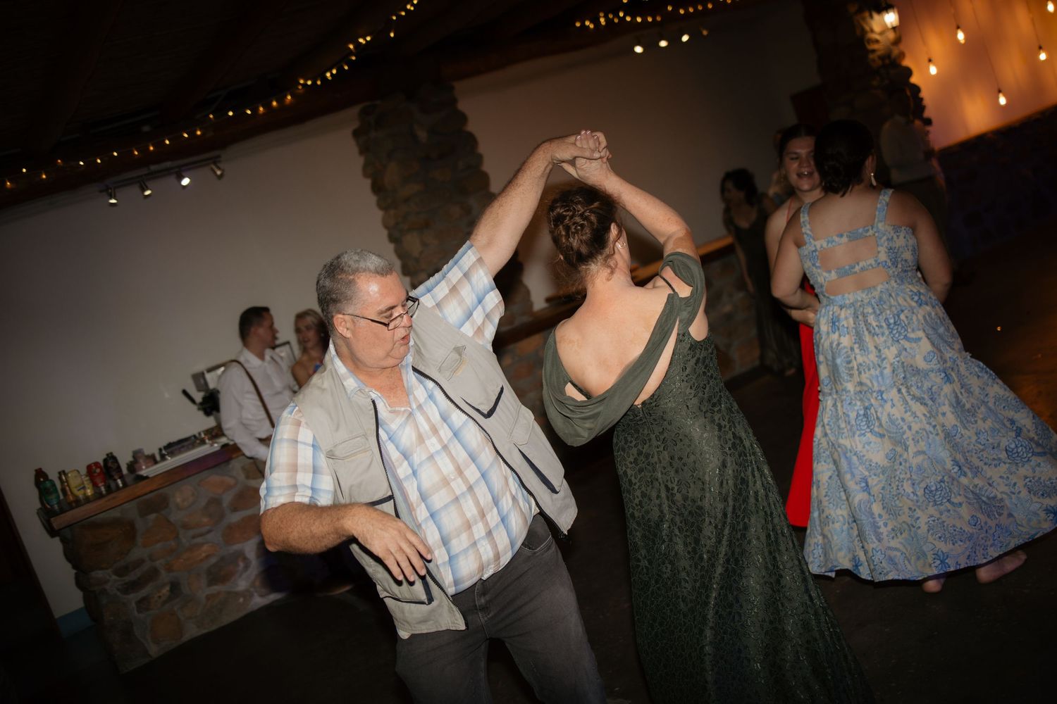Guests dancing joyfully at a warmly lit rustic wedding reception venue.