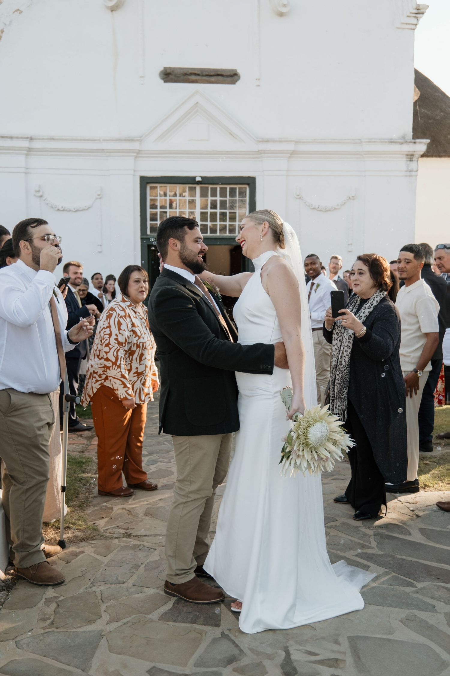 Wedding reception guests mingling on stone patio outside Tulbagh Church