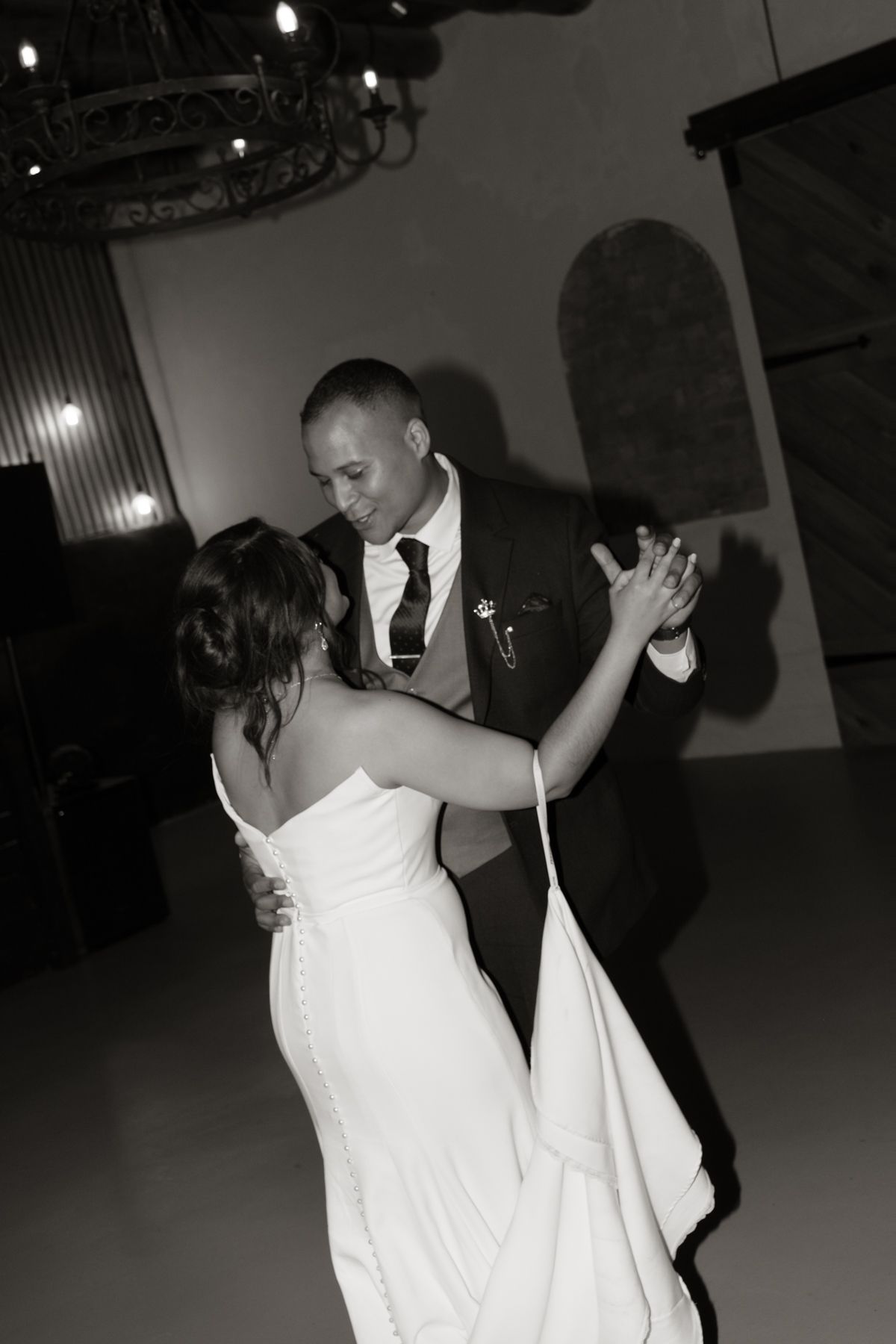 Black and white photo of bride and groom sharing their first dance at a rustic wedding venue.
