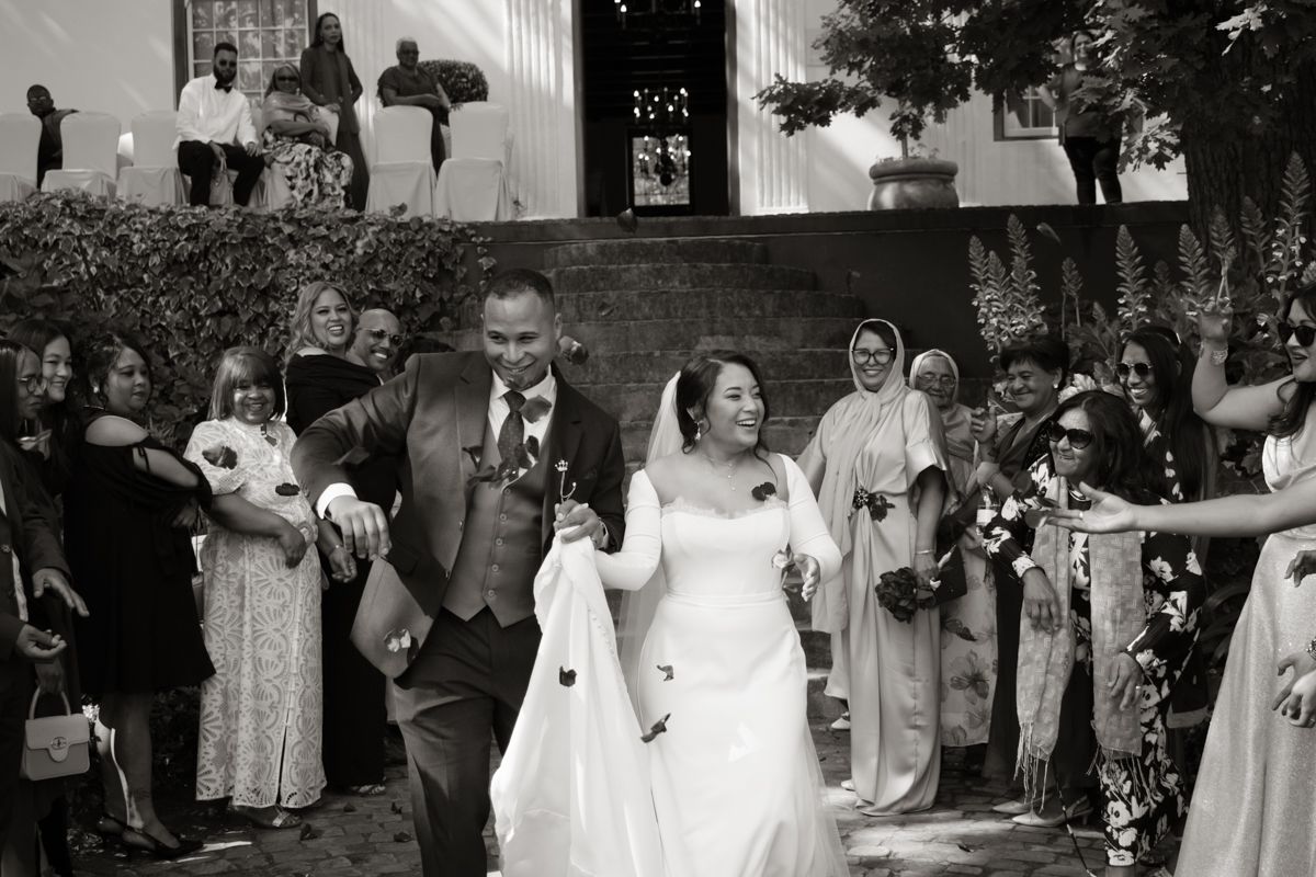 Bride and groom exit church ceremony through cheering guests in classic black and white wedding photo.
