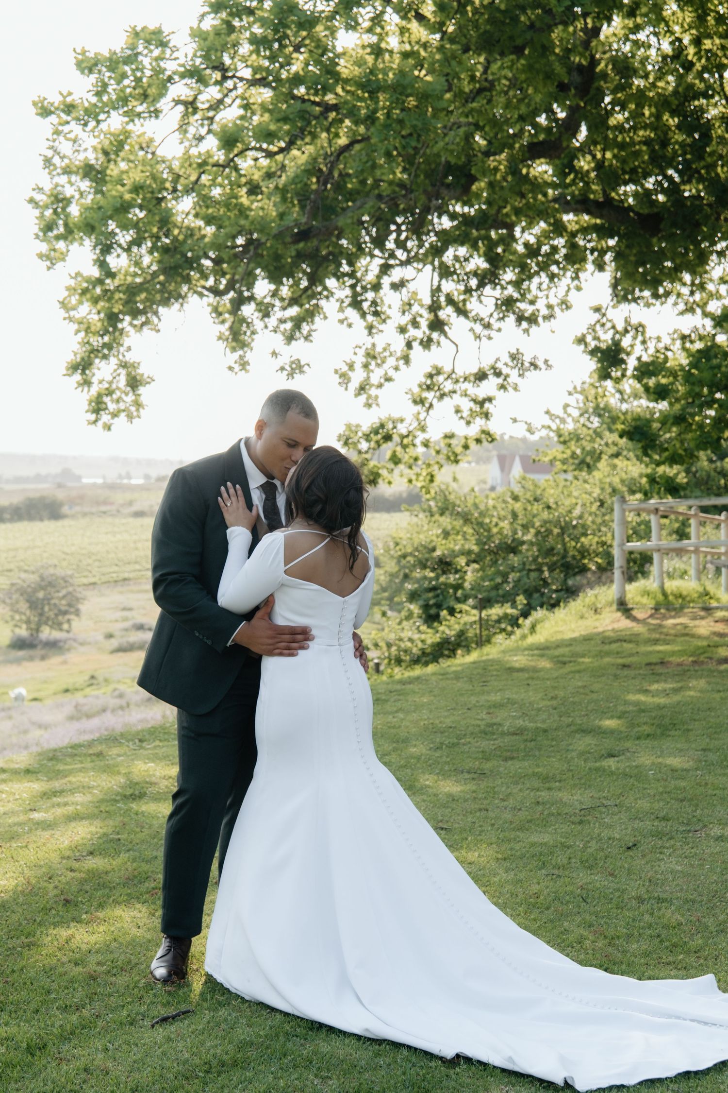 Bride and groom share a romantic kiss outdoors on green lawn with trees in background at wedding.