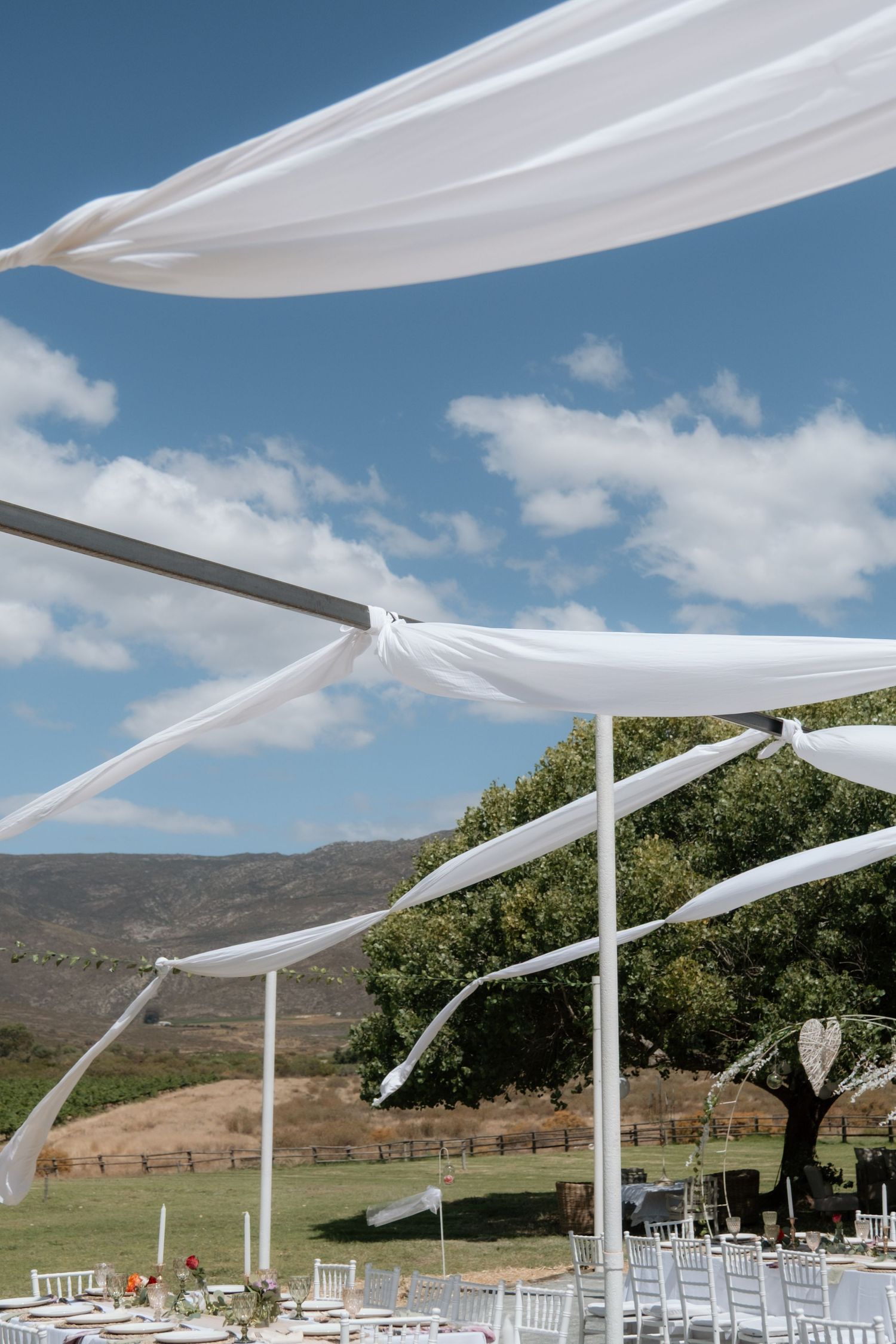 White fabric draping billows in the wind over an outdoor wedding reception setup with mountain views.