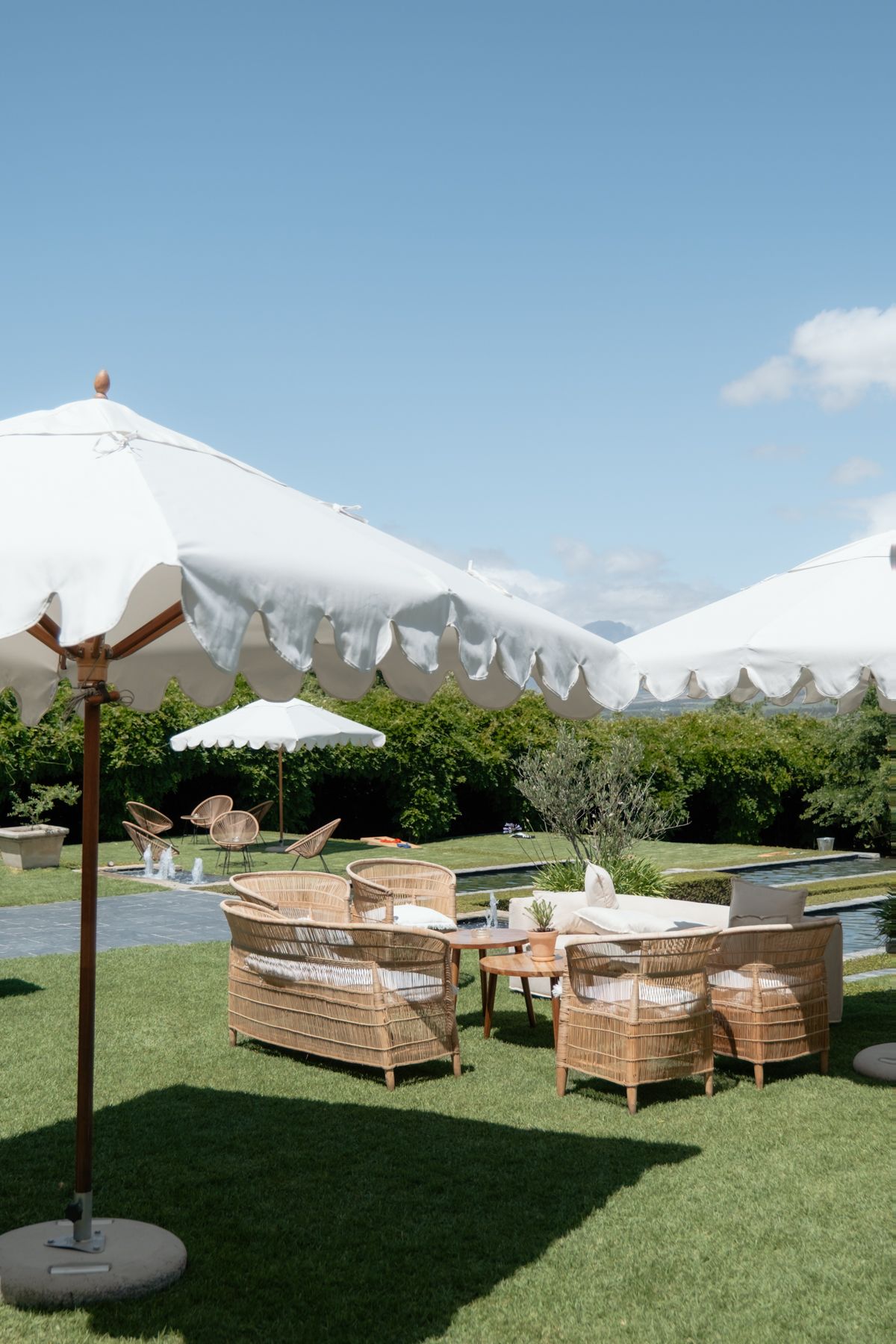 Outdoor wedding venue with rattan furniture and white fringed umbrellas on a sunny day.