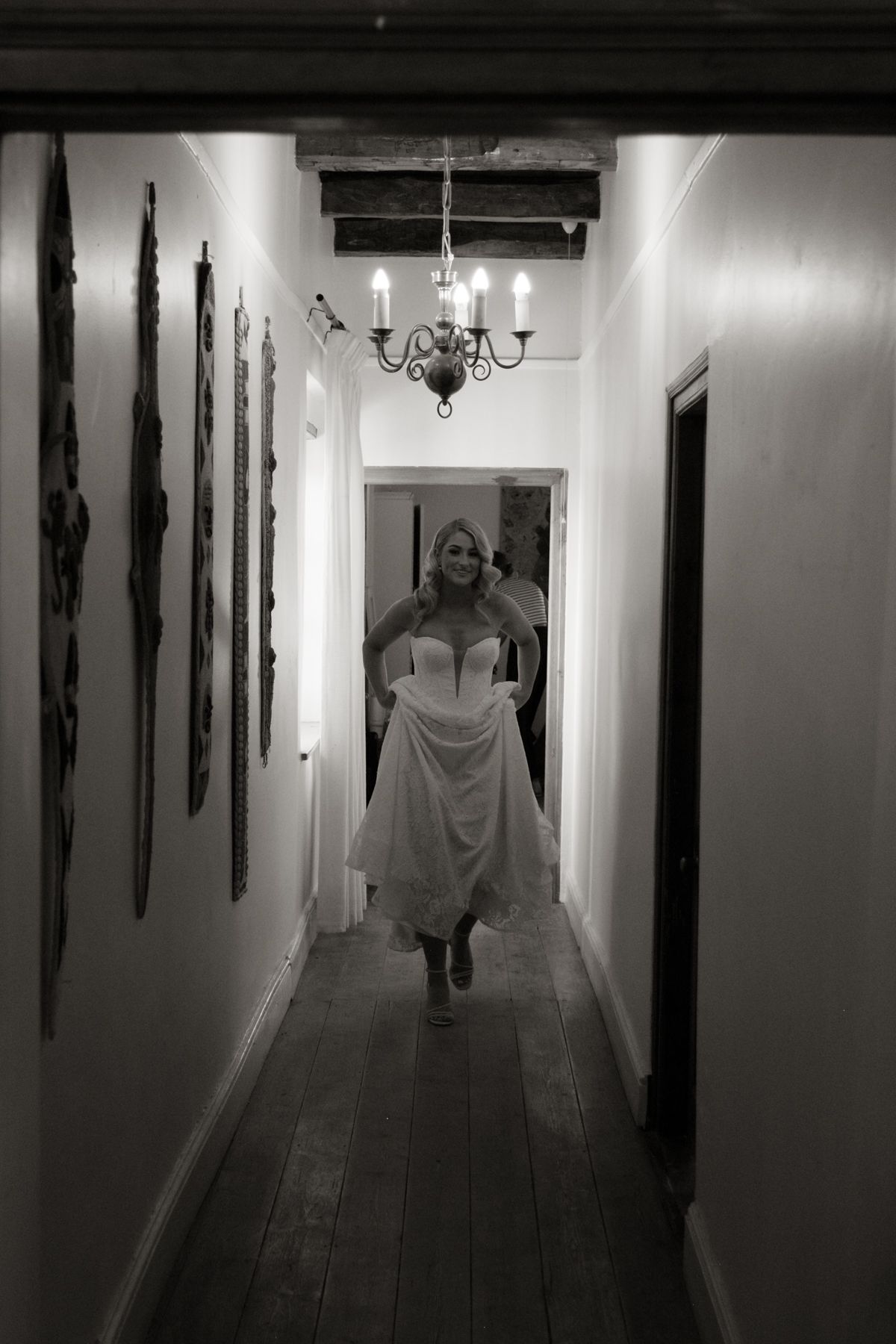 Black and white photo of bride walking down hallway in strapless wedding gown at rustic venue.