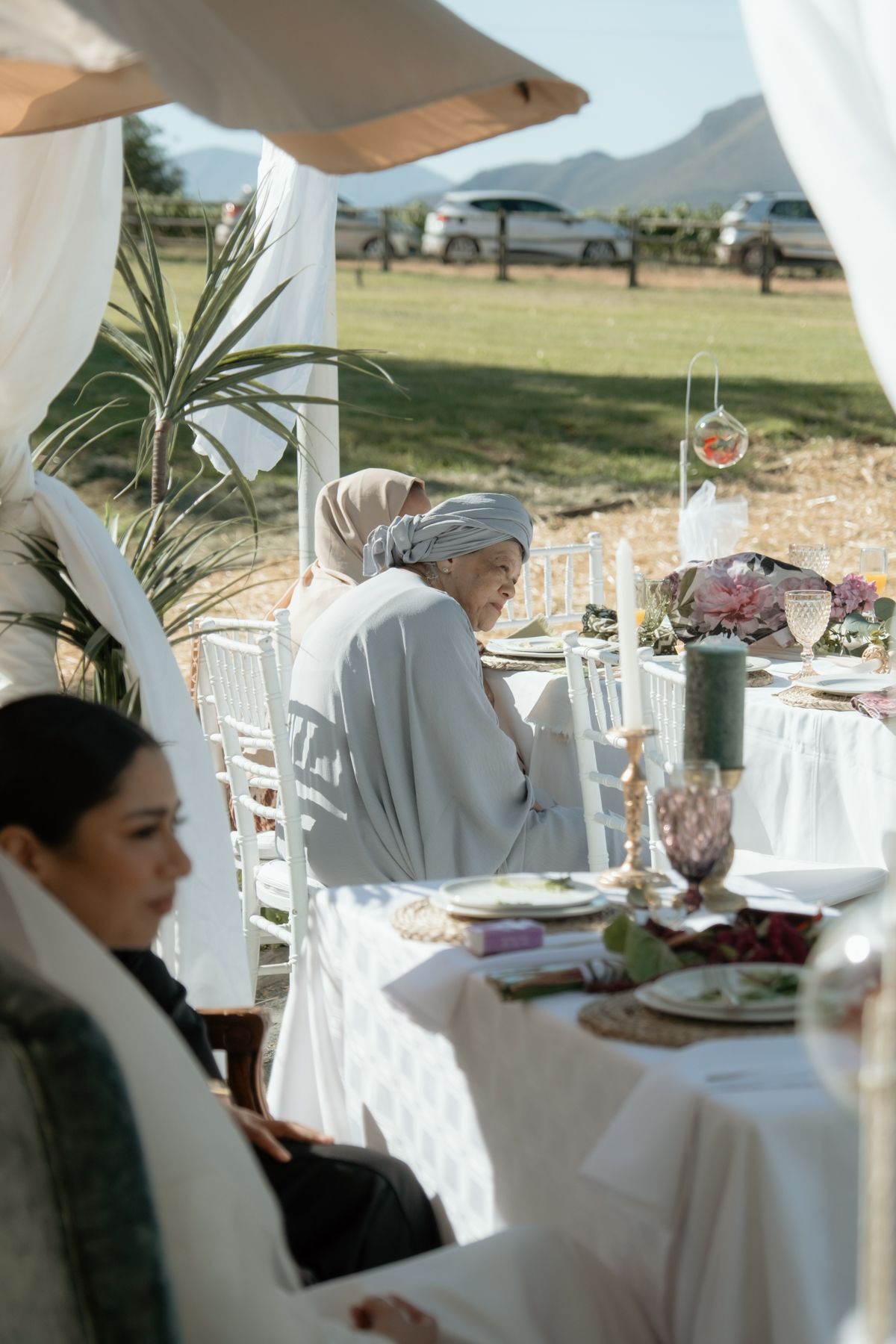 Women in hijabs seated at an elegant outdoor wedding reception table with floral decor and mountain views.