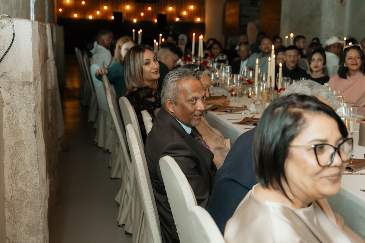 Wedding reception guests seated along an elegantly decorated long table with candles and floral centerpieces.