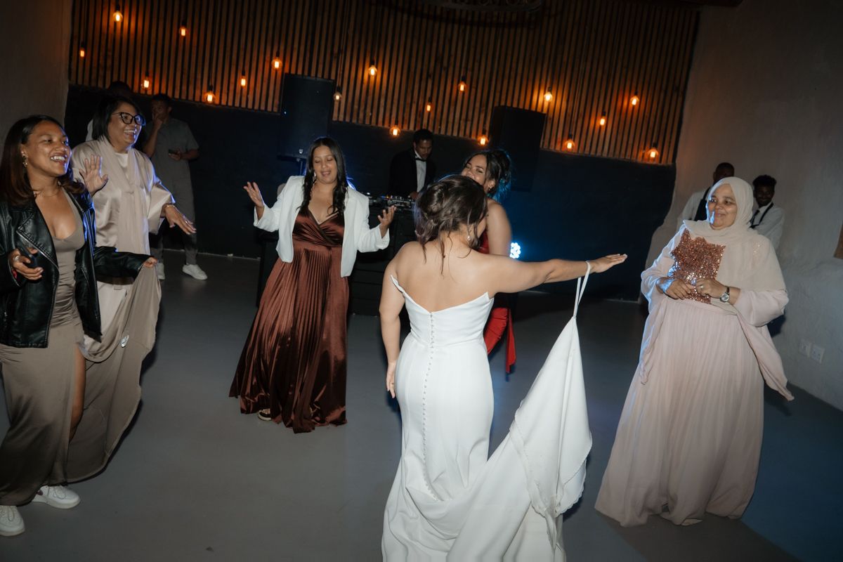 Bride in white gown dancing joyfully with guests in elegant attire at wedding reception dance floor.