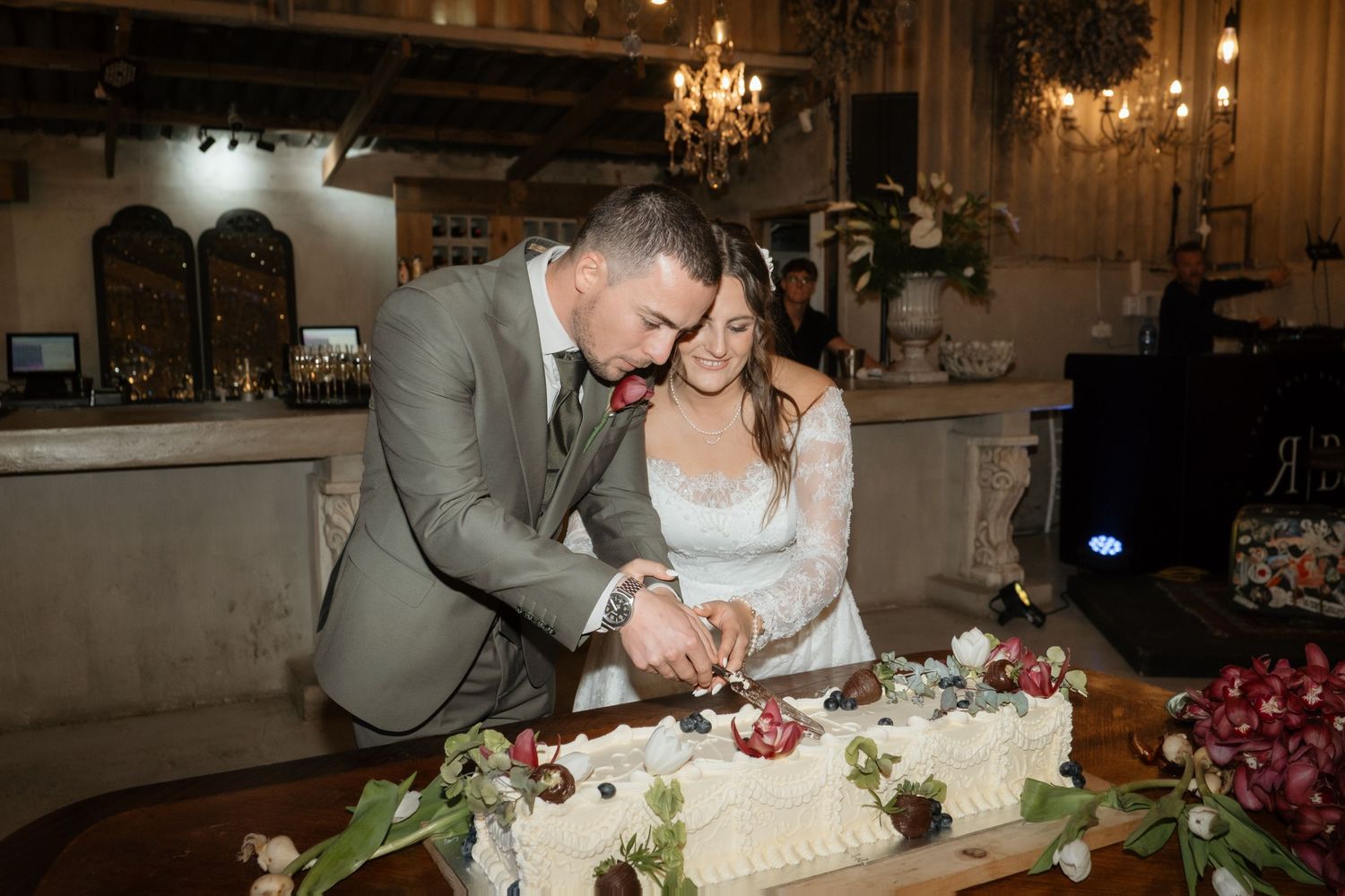 Bride and groom cutting white rectangular wedding cake decorated with flowers at reception.