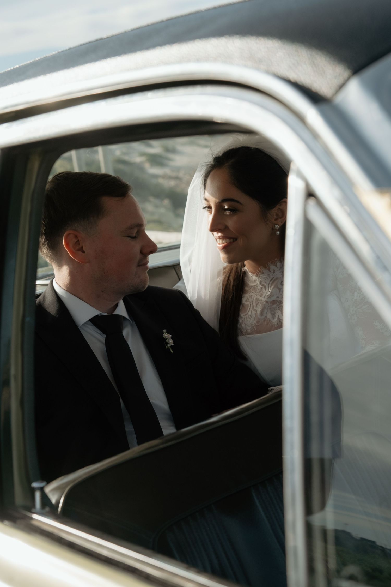 Bride and groom share a romantic moment inside a vintage car on their wedding day.