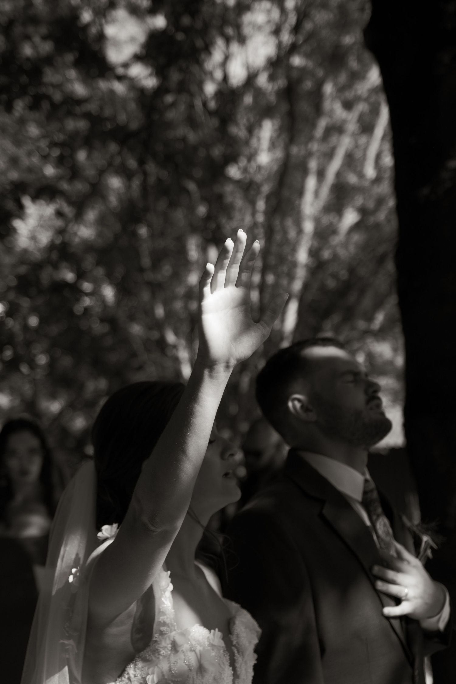 Bride raises hand during outdoor wedding ceremony in black and white photo.