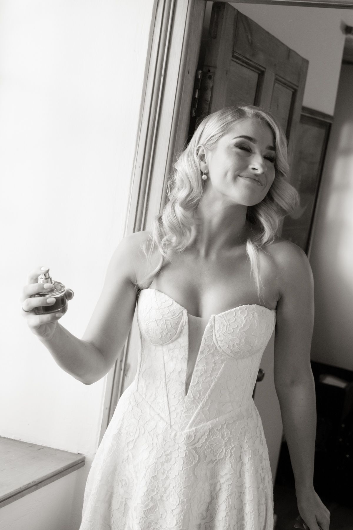 Smiling bride in strapless lace wedding gown holding a cupcake, black and white portrait.