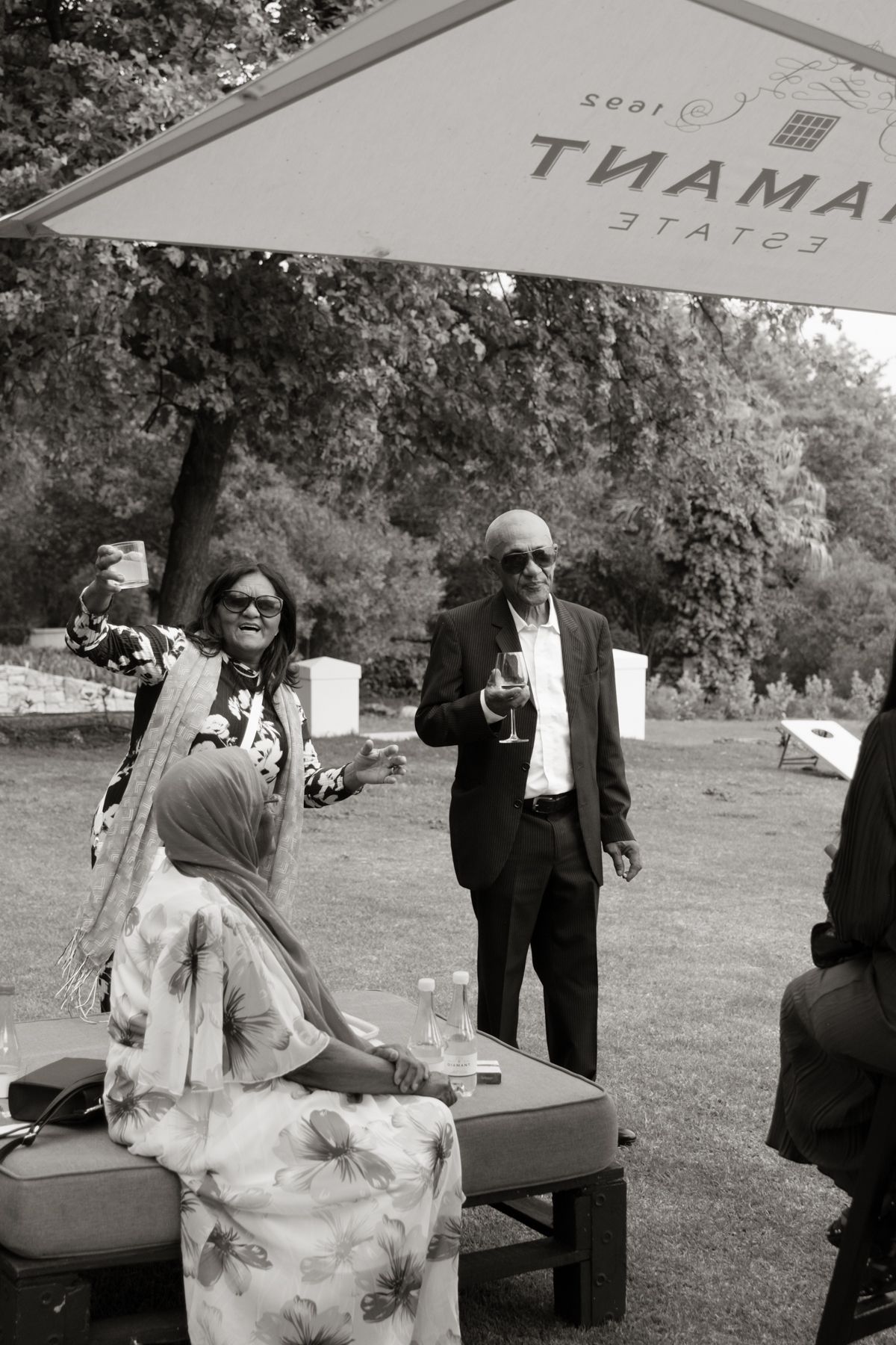 Black and white photo of wedding guests socializing under umbrellas at Diamant Estate reception.