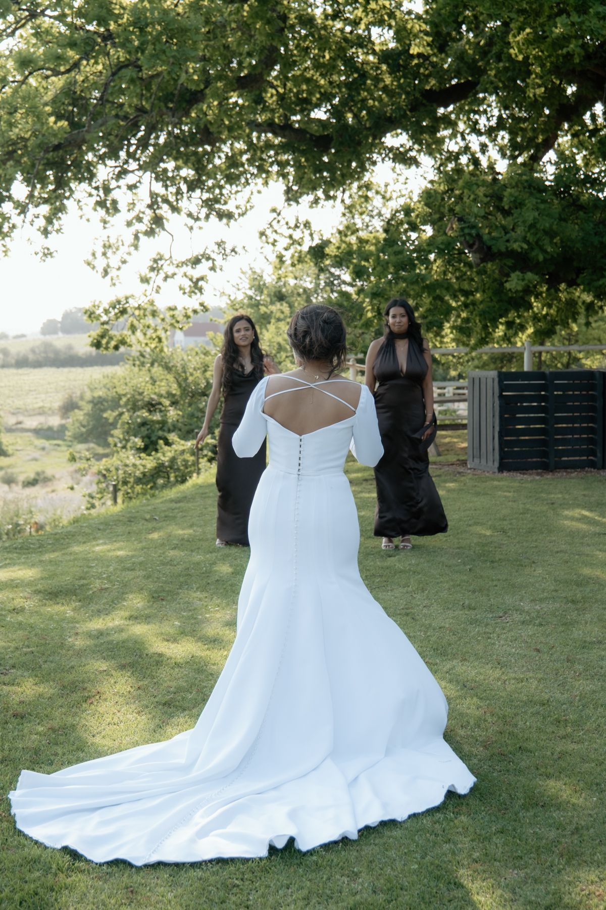 Elegant bride in fitted white gown with open back and train standing in garden setting.