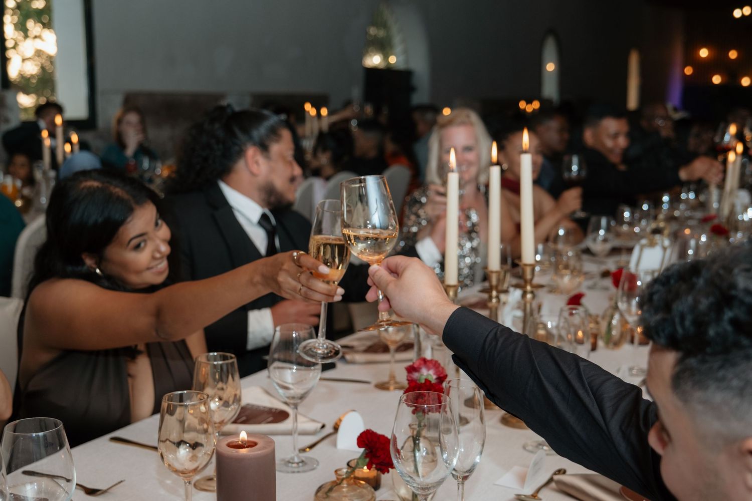 Wedding guests raising champagne glasses in a toast at an elegant candlelit reception dinner.