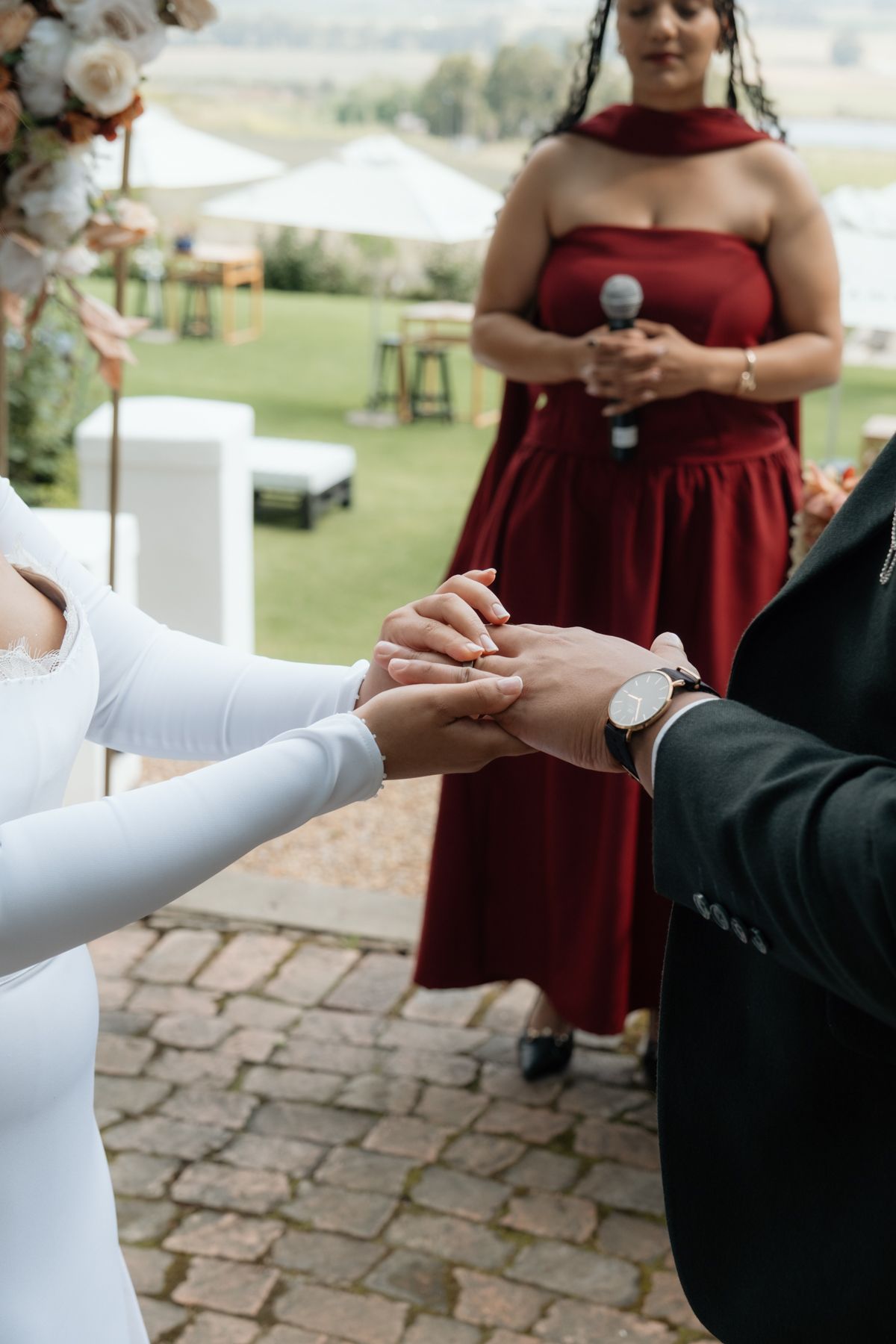 Bride placing wedding ring on grooms hand during outdoor ceremony with officiant.