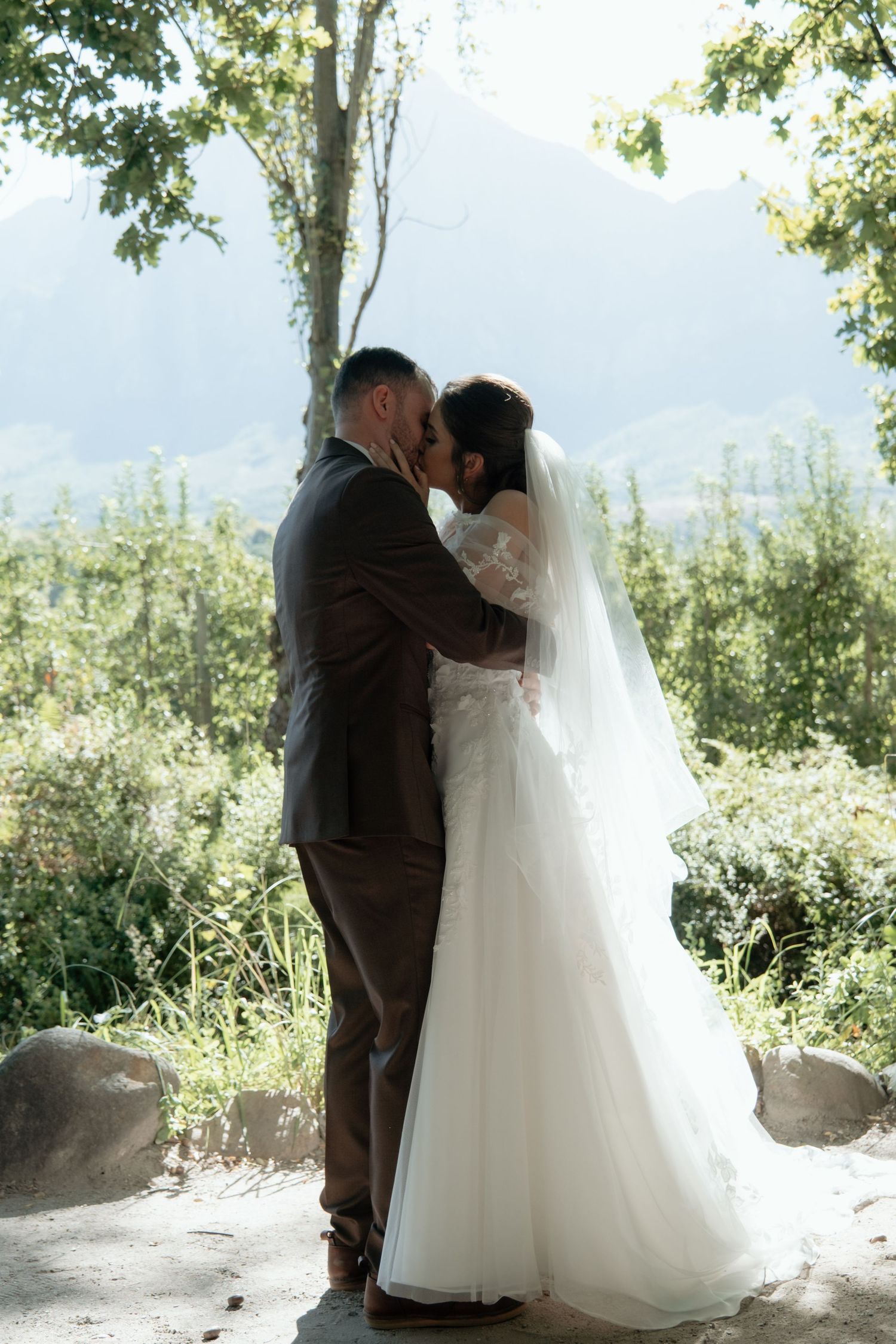 Bride and groom share romantic kiss outdoors with mountain landscape behind them.