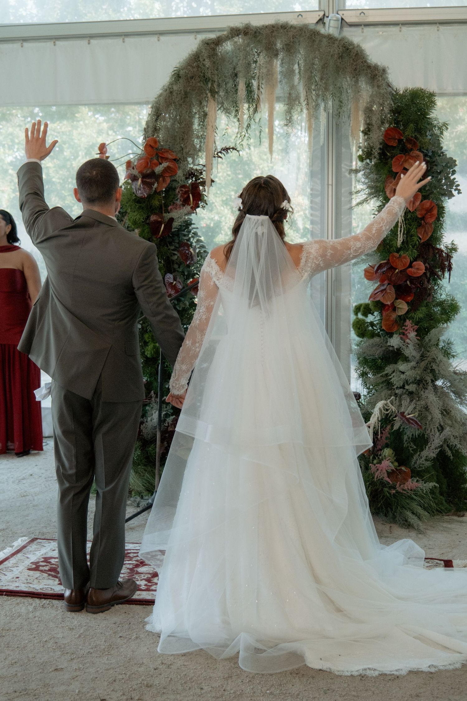 Bride and groom raising hands at floral arch during outdoor tent wedding ceremony.