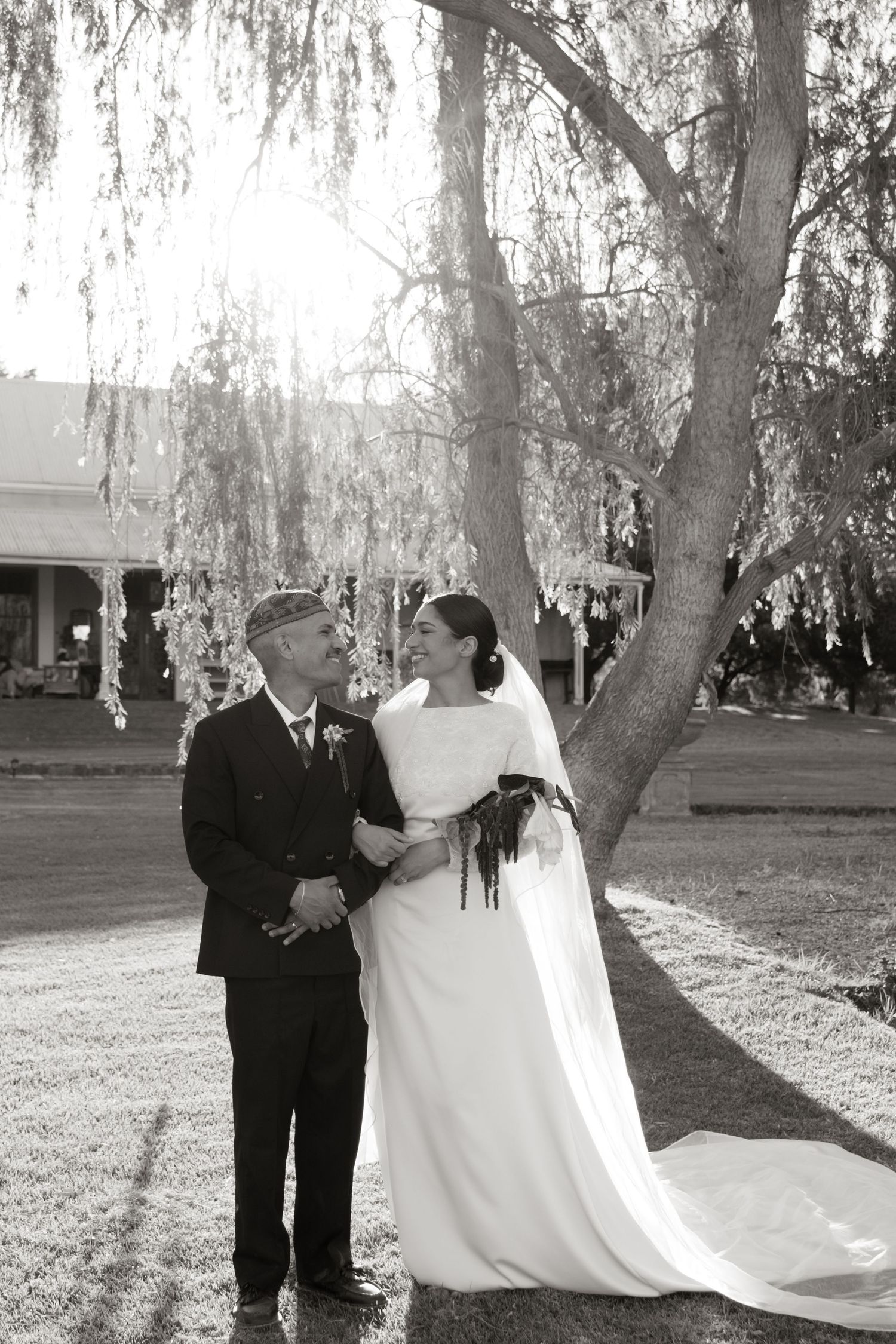 Black and white photo of bride and groom sharing a romantic moment under a willow tree at their outdoor wedding.