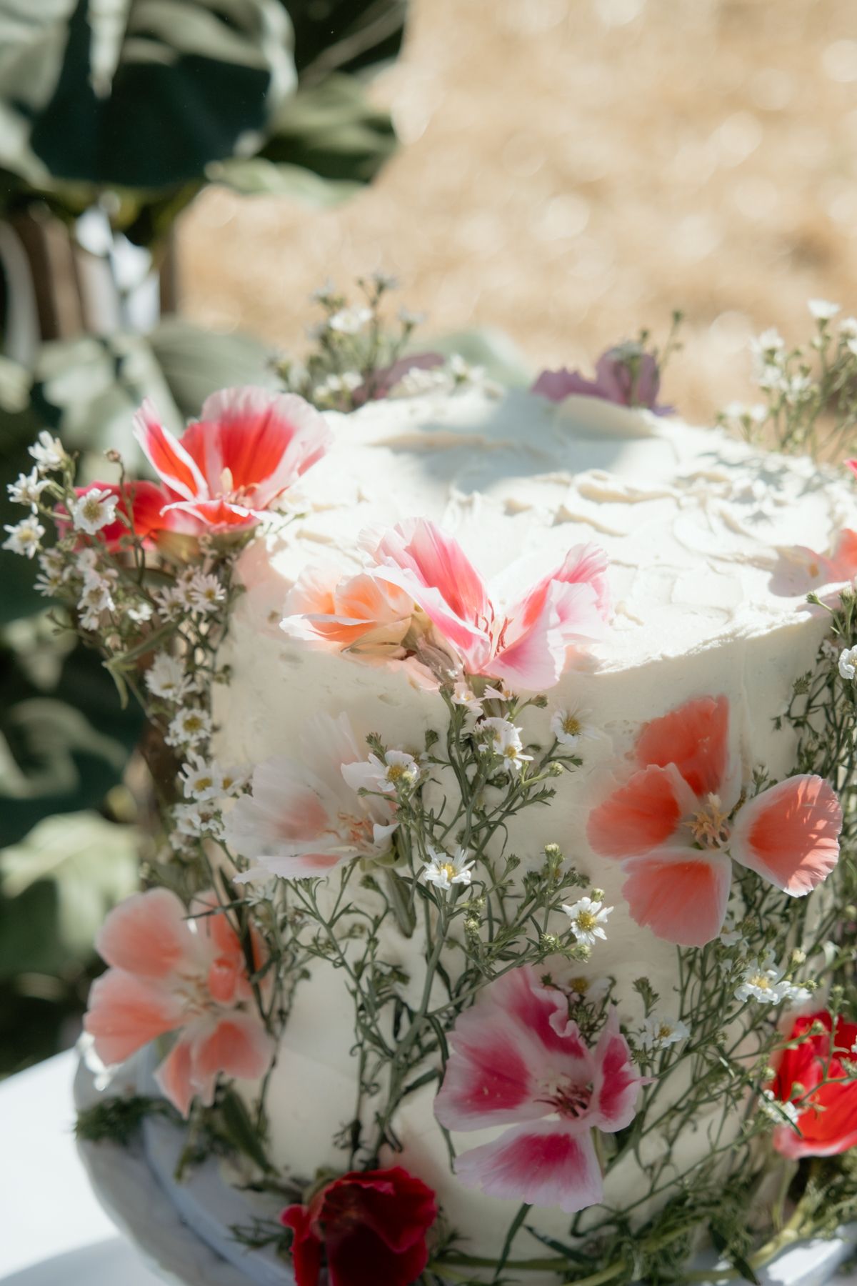 Elegant white wedding cake decorated with pink and red fresh flowers and baby's breath blooms.