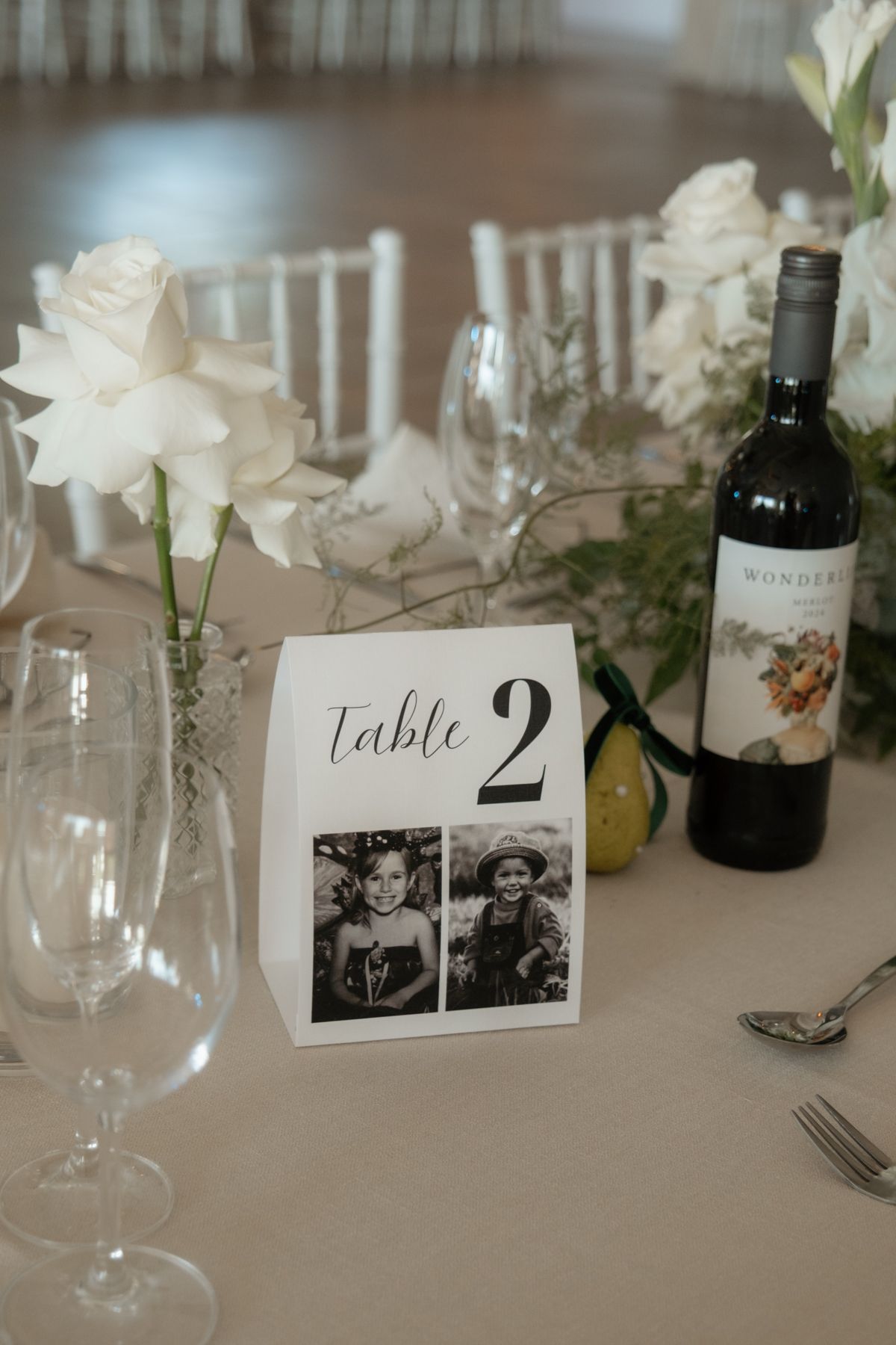 Elegant wedding table setting with Table 2 card, white flowers, wine bottle and crystal glassware.