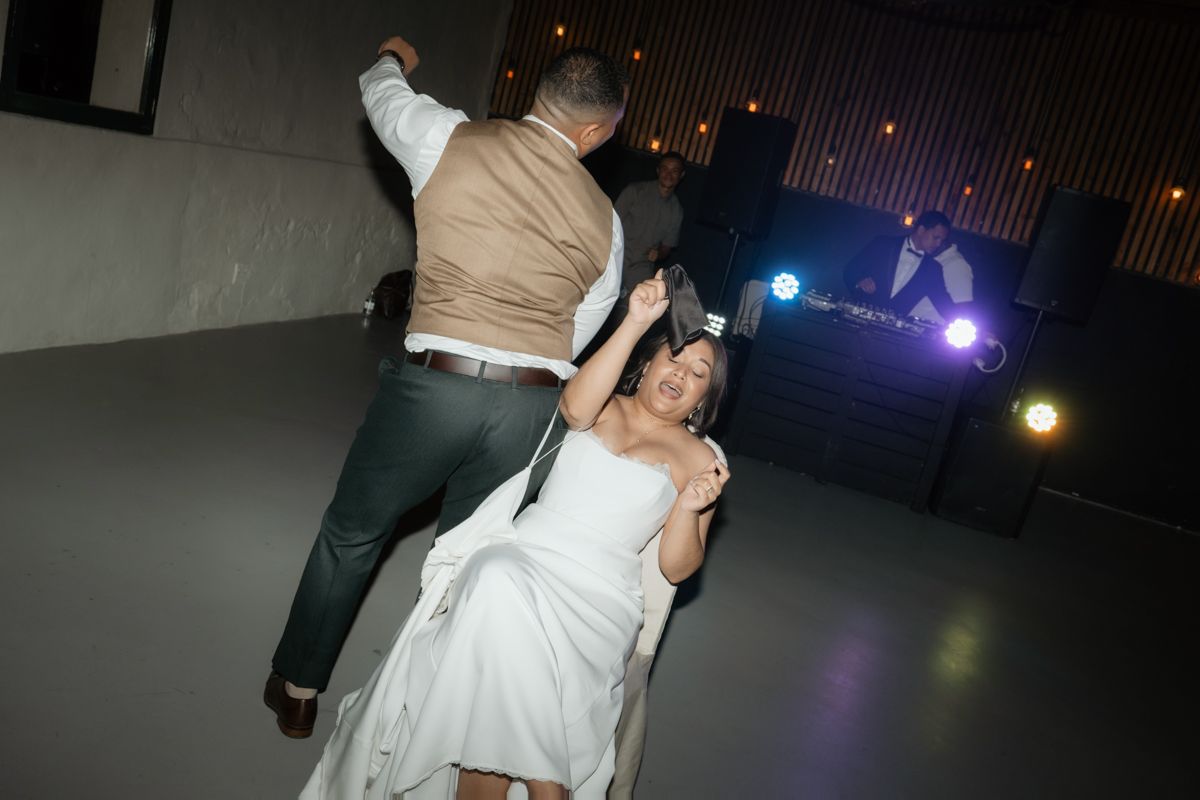 Bride in white dress being dipped by groom on the dance floor at a lively wedding reception.