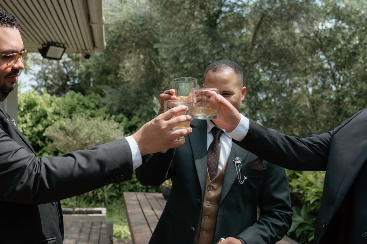 Groomsmen clinking glasses in a celebratory toast outdoors before the wedding ceremony.