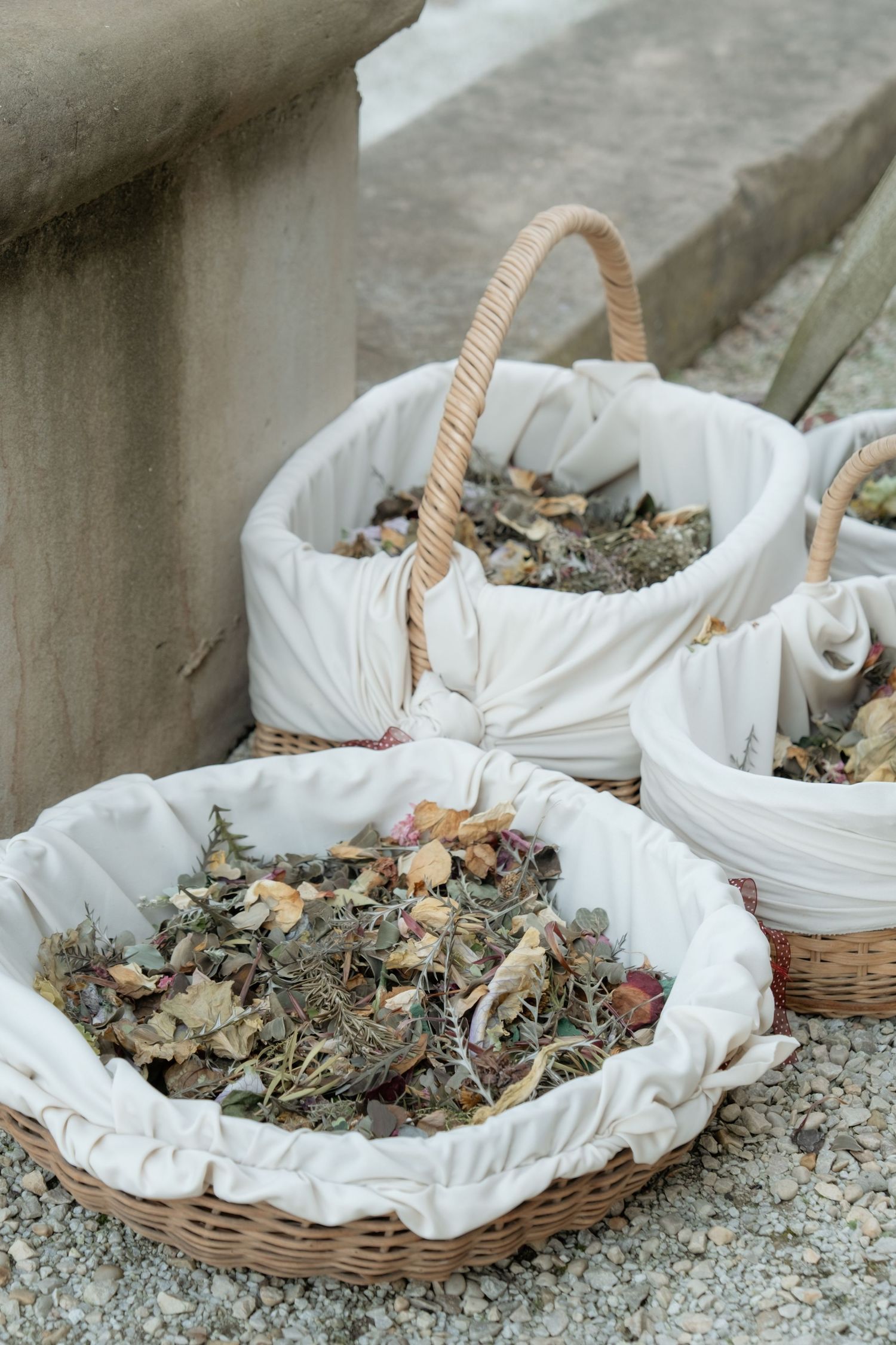 Wicker baskets lined with white fabric filled with dried flower petals for wedding ceremony confetti.