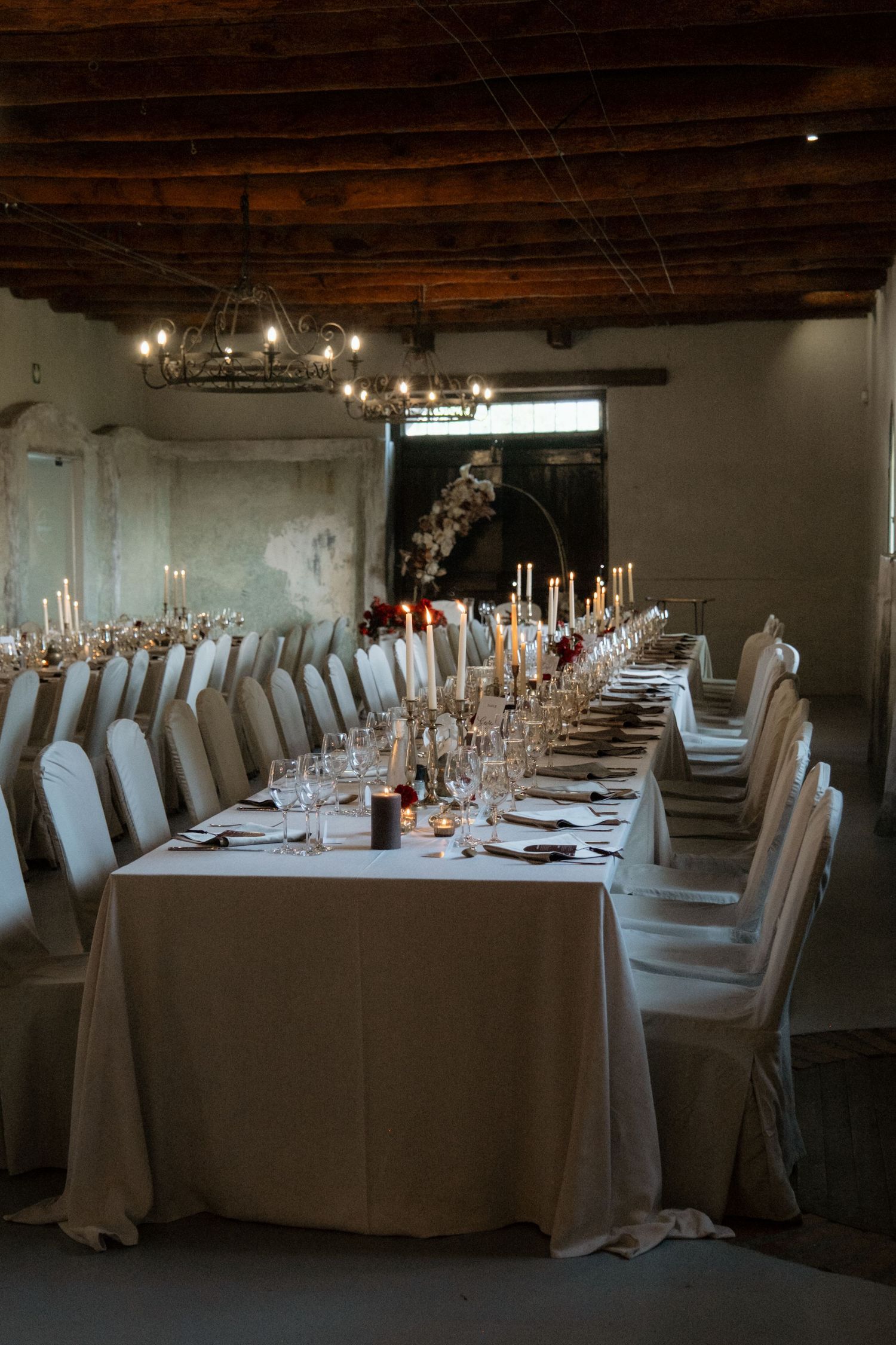 Elegant wedding reception hall with long dining table, candles, and rustic wood ceiling.