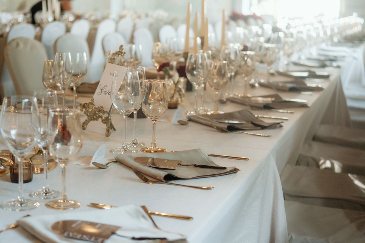 Elegant wedding reception table set with crystal glassware, gold candlesticks, and white linen in soft lighting.