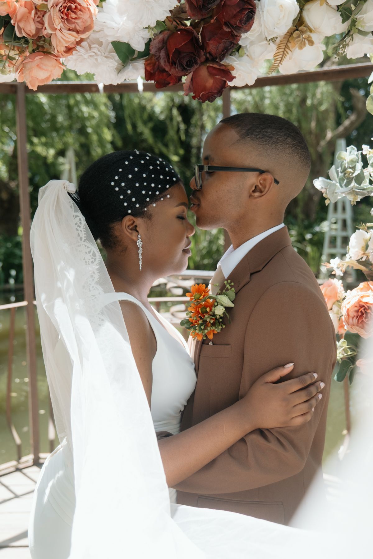 Bride and groom sharing an intimate moment under a stunning floral wedding arch with orange and white blooms.