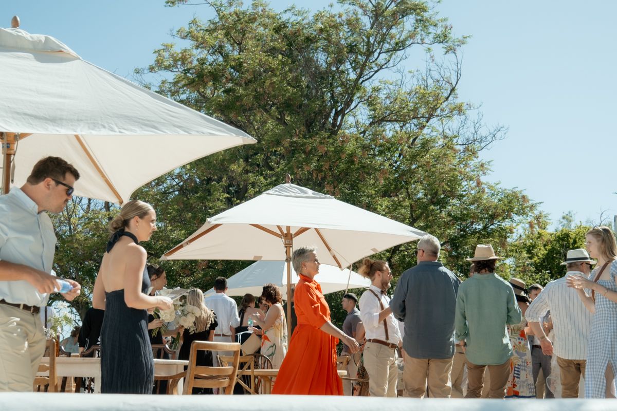 Wedding guests mingling outdoors under white parasols on a sunny day at an elegant garden reception.