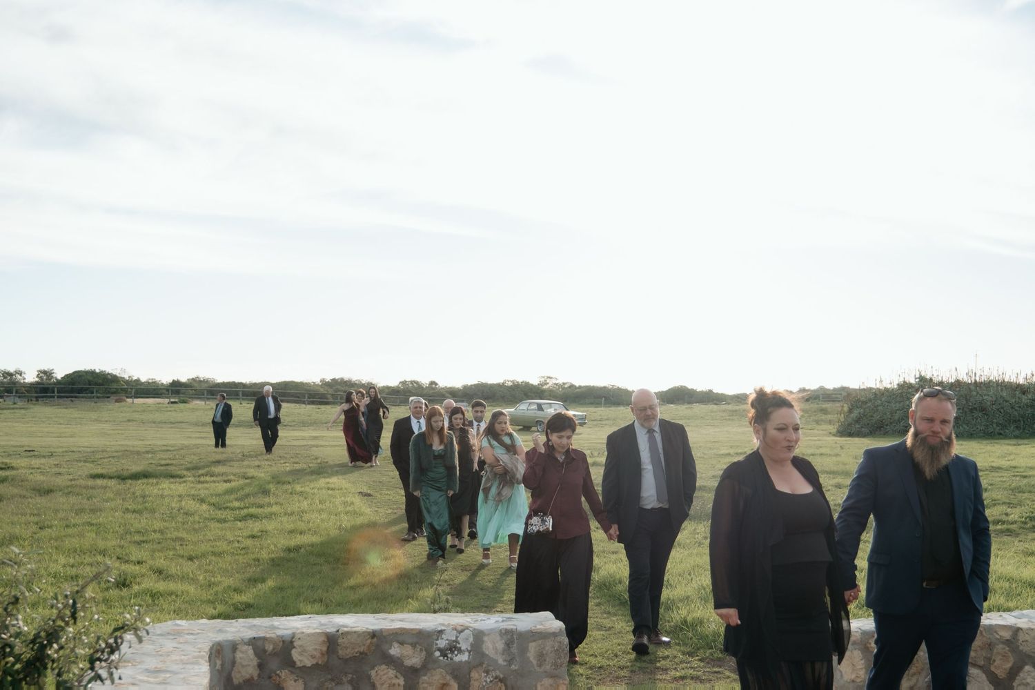 Group of wedding guests walking across a scenic green field at dusk during an outdoor ceremony.