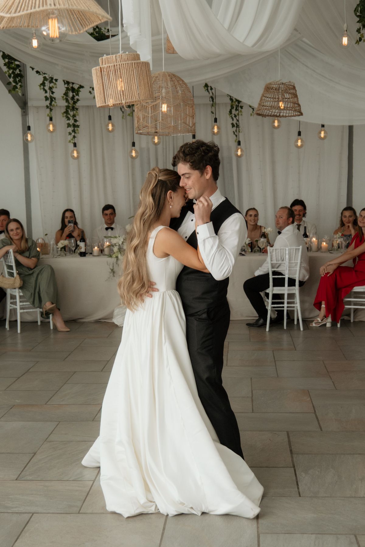 Bride and groom share first dance under warm bistro lights at elegant reception.