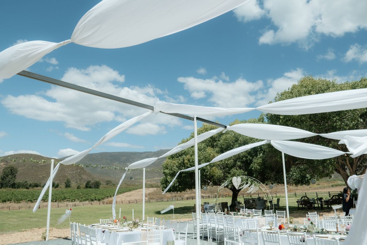Elegant outdoor wedding reception with white draped canopy and vineyard mountain backdrop.
